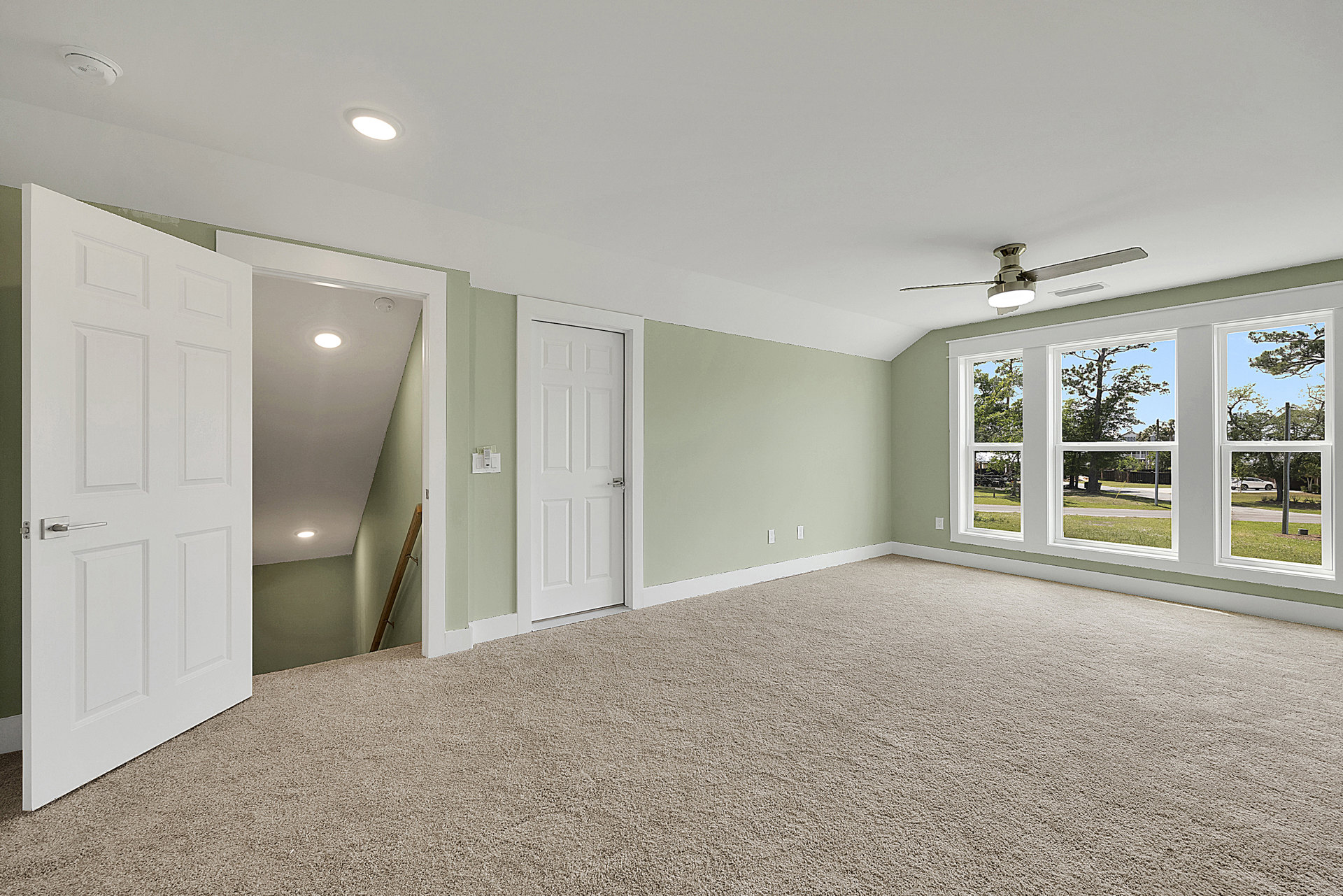 Carpeted room with white paneled doors, ceiling fan with light fixture, window, and wooden door frame with metal handle