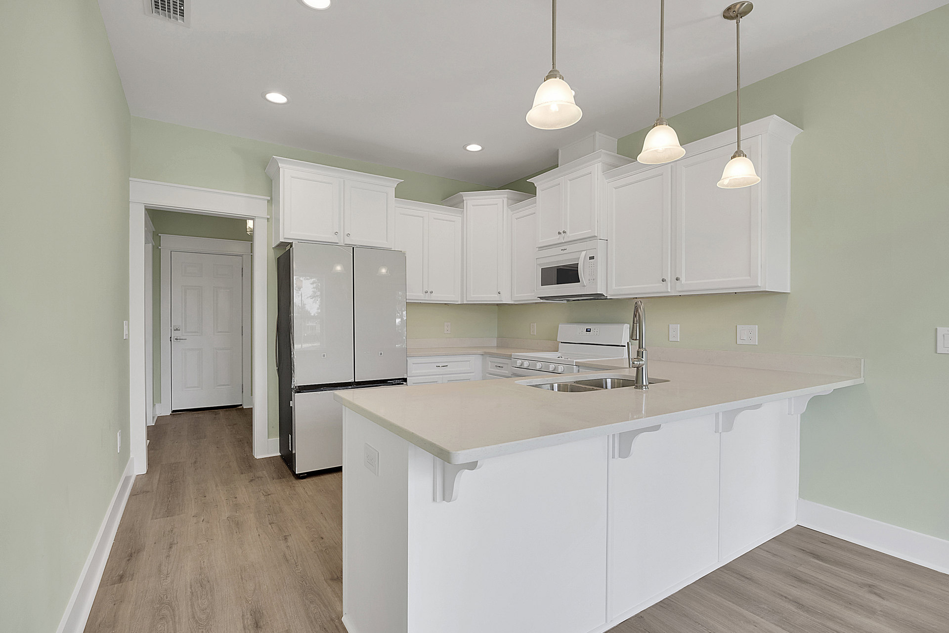 Kitchen with white shaker cabinets, white quartz island, stainless sink, white refrigerator wrapped in plastic, white microwave with glass door, tile floor, metal pole mounted on