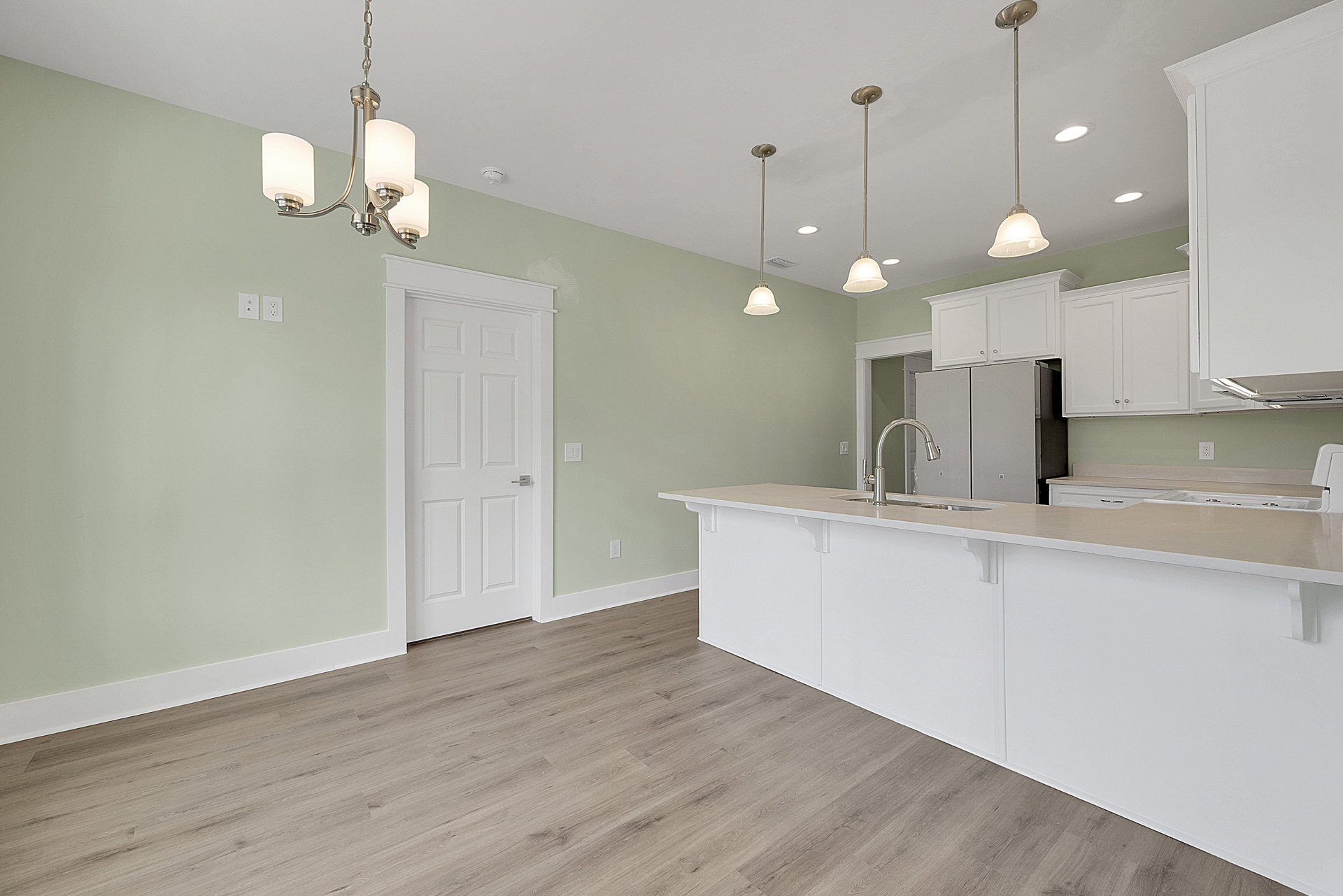 Kitchen with white island, wood plank flooring, white walls, stainless steel faucet, pendant light fixture, and silver door handle