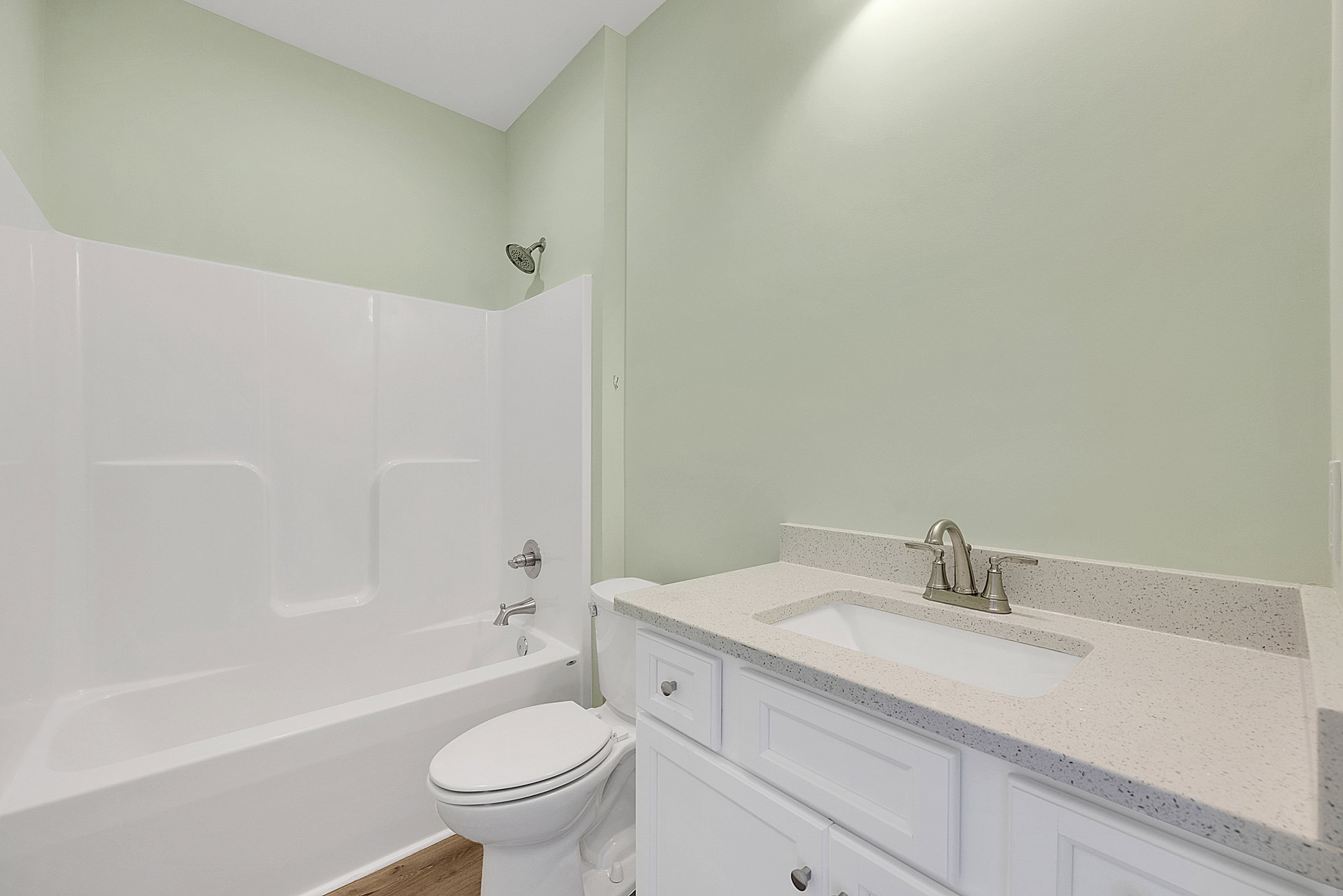 Modern bathroom with white toilet, built-in bathtub, wall-mounted shower head, light tile walls, under-sink cabinets, chrome faucet, and integrated sink