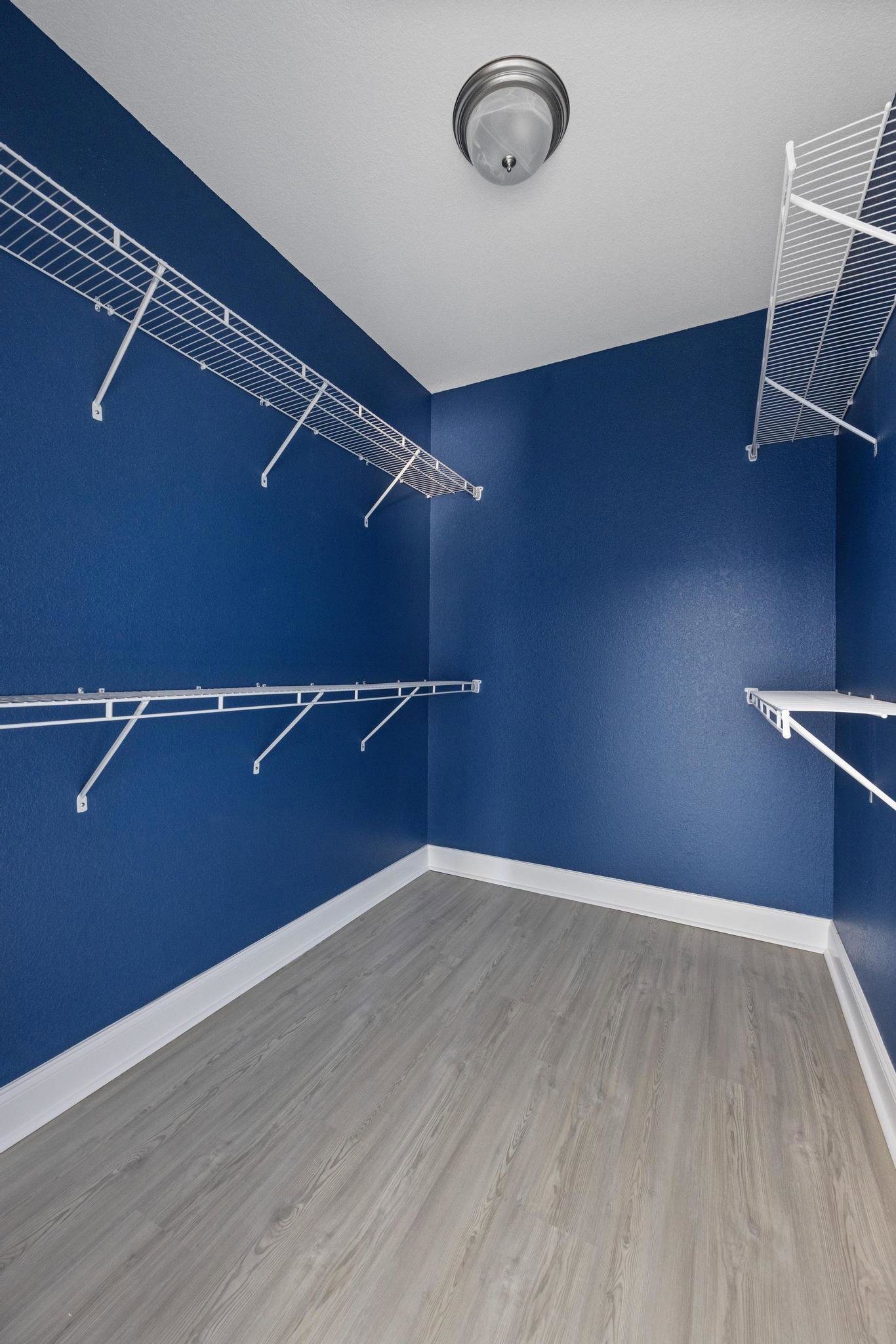 Built-in white shelves line a blue accent wall in a room with wood flooring, white metal railing, and a modern ceiling light fixture.
