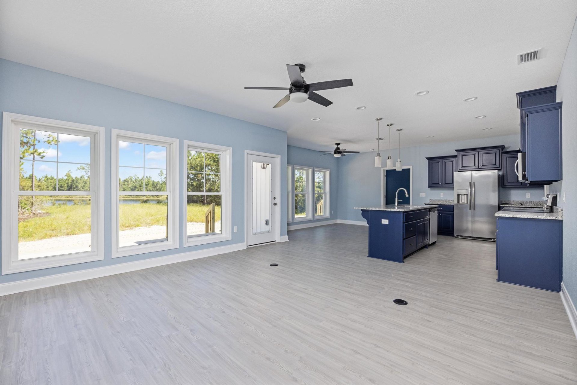 Open-concept kitchen and living area featuring a central island with white cabinetry, stainless steel refrigerator with water dispenser, ceiling fan with light fixture, blue accent