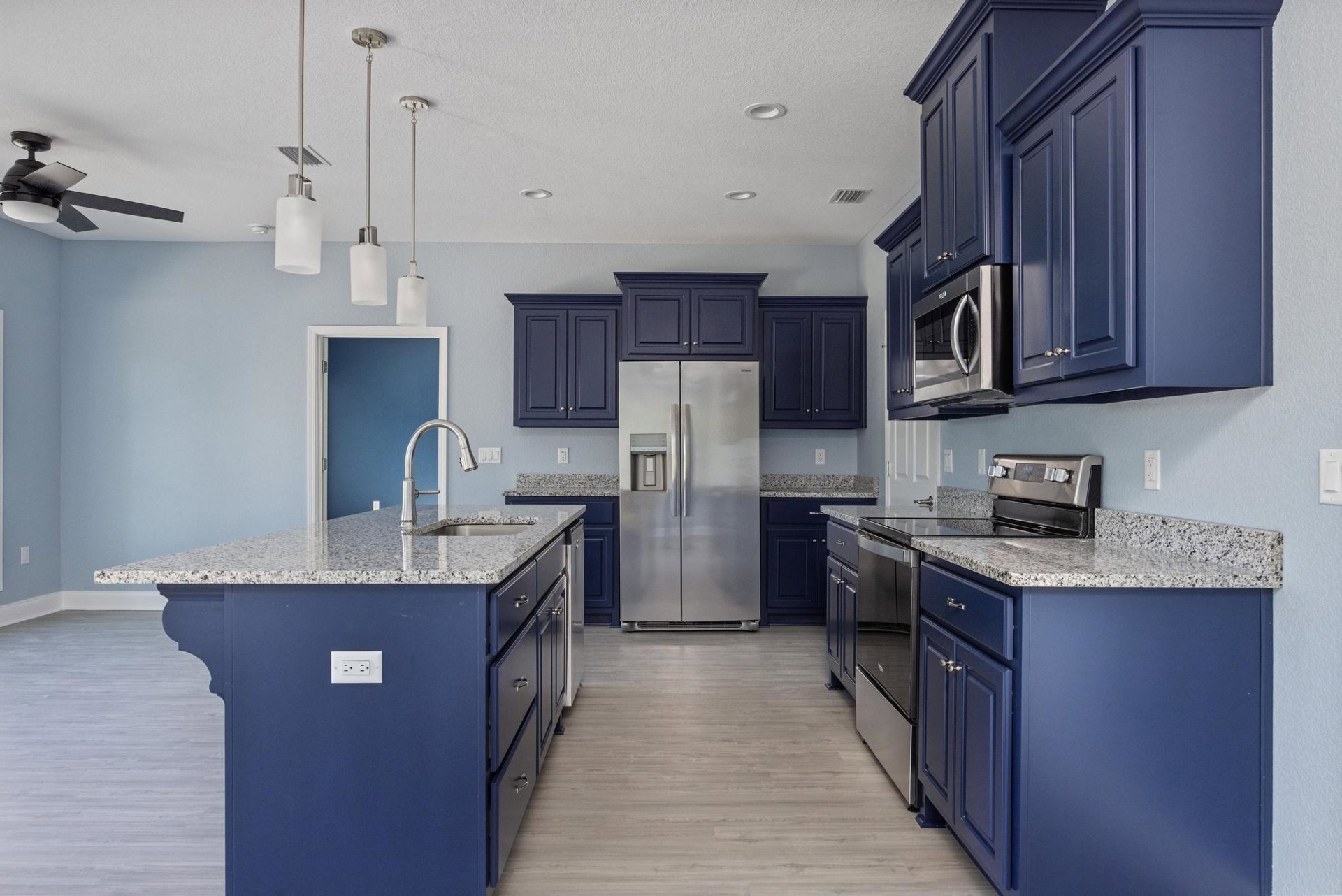 Blue kitchen cabinets with granite countertops, stainless steel refrigerator with water dispenser, built-in microwave above cabinetry, stove, and tiled floor