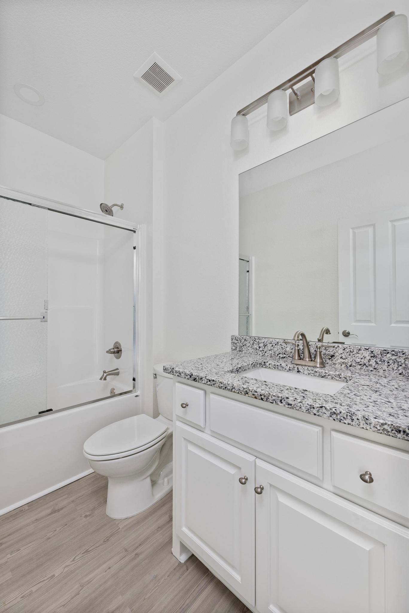Bathroom featuring a marble countertop vanity, glass-enclosed shower with tile walls, white toilet, and recessed lighting fixture
