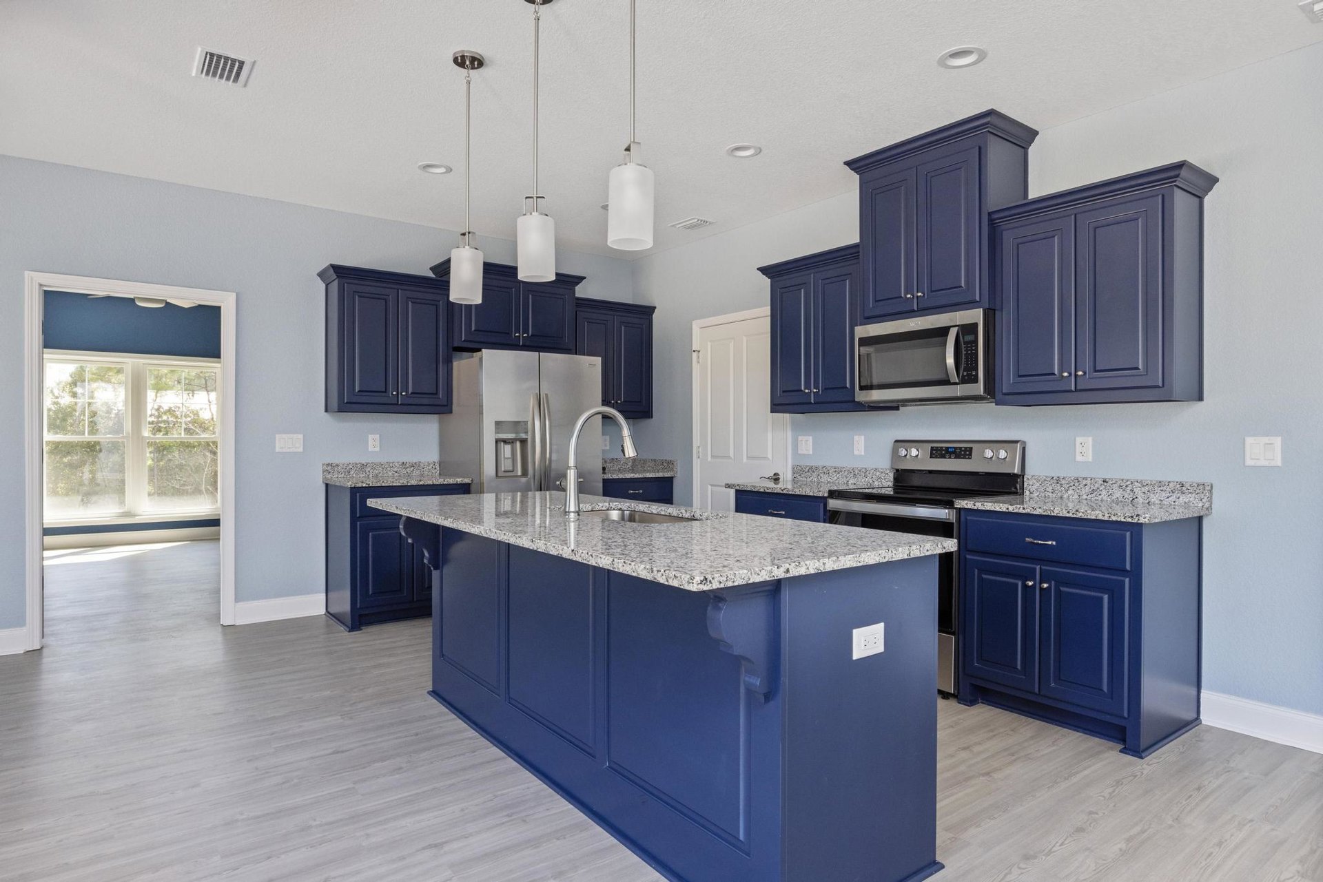 Blue kitchen cabinets, granite island countertop, open microwave door, white outlet on blue wall, white ceiling fan, lighted rectangular object, hardwood flooring