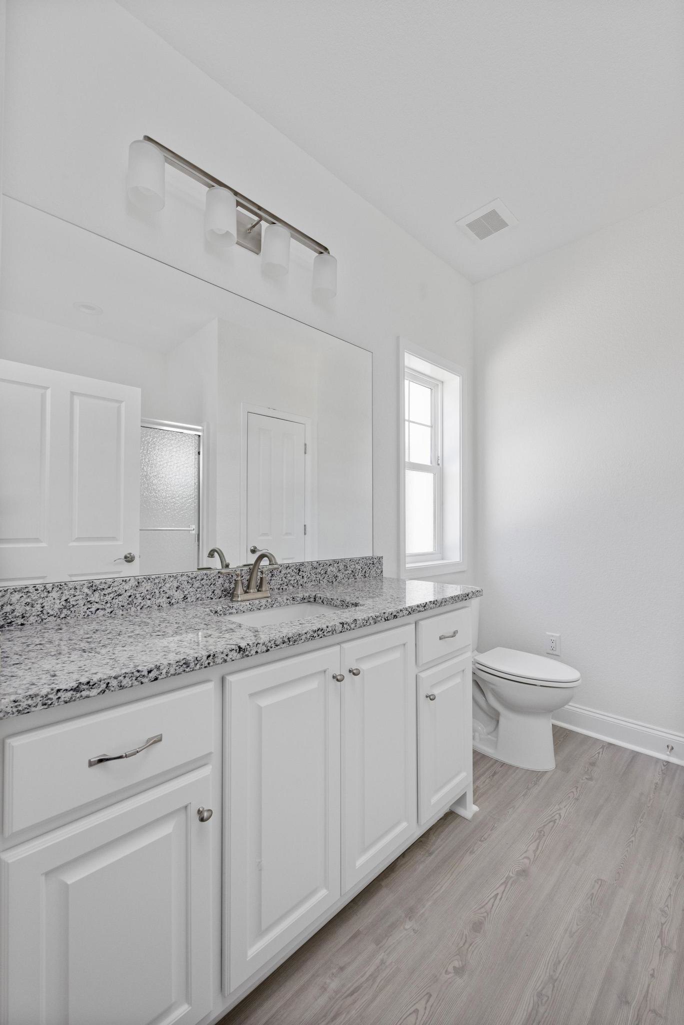Bathroom with marble countertop, white toilet, white cabinetry, metal door handle, tile flooring, and window