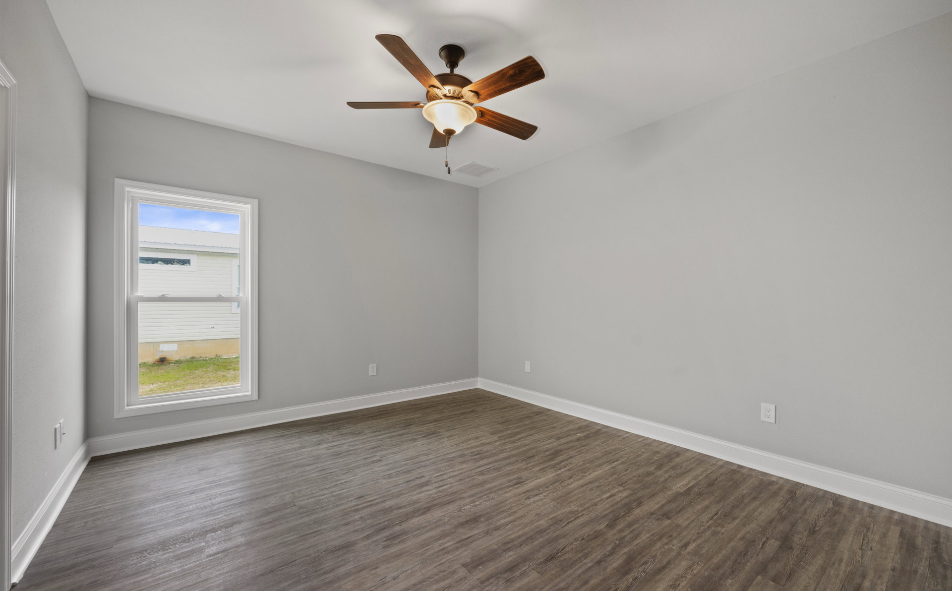 Ceiling fan with light fixture mounted on white plaster ceiling, wood laminate flooring, large window revealing exterior house, bright indoor room