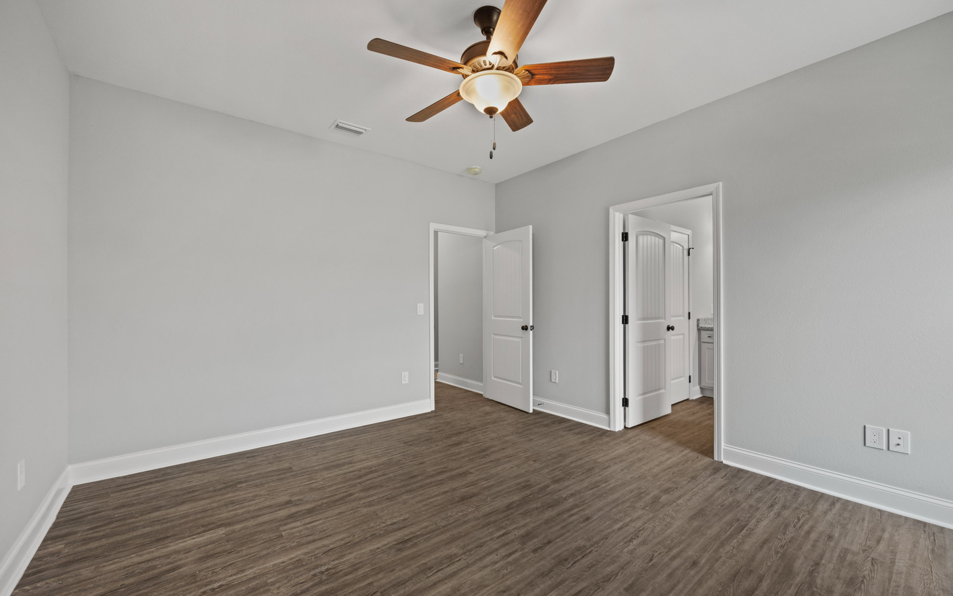 Ceiling fan with integrated light fixture above wood flooring, white walls, and a white door with black knobs