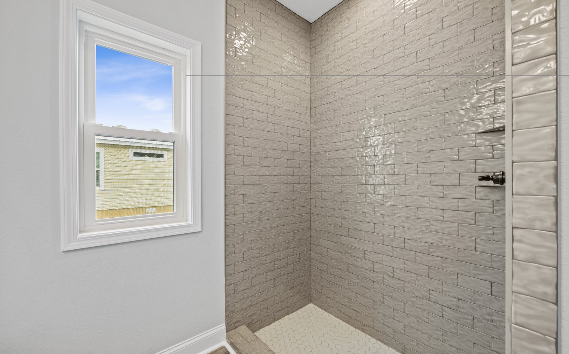 Tiled shower featuring a white-framed window with blue sky view, white tile floor, and brown accent wall