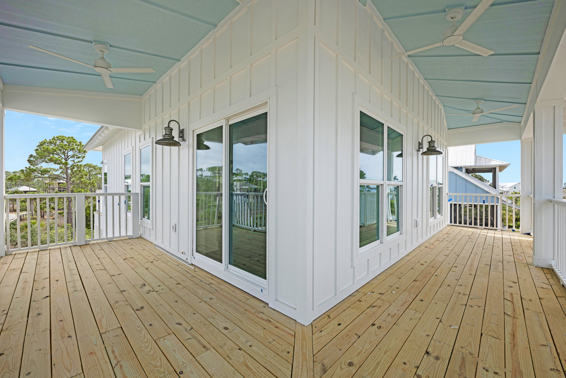 White house exterior with blue porch ceiling, wooden deck, white railing, and window on white wall