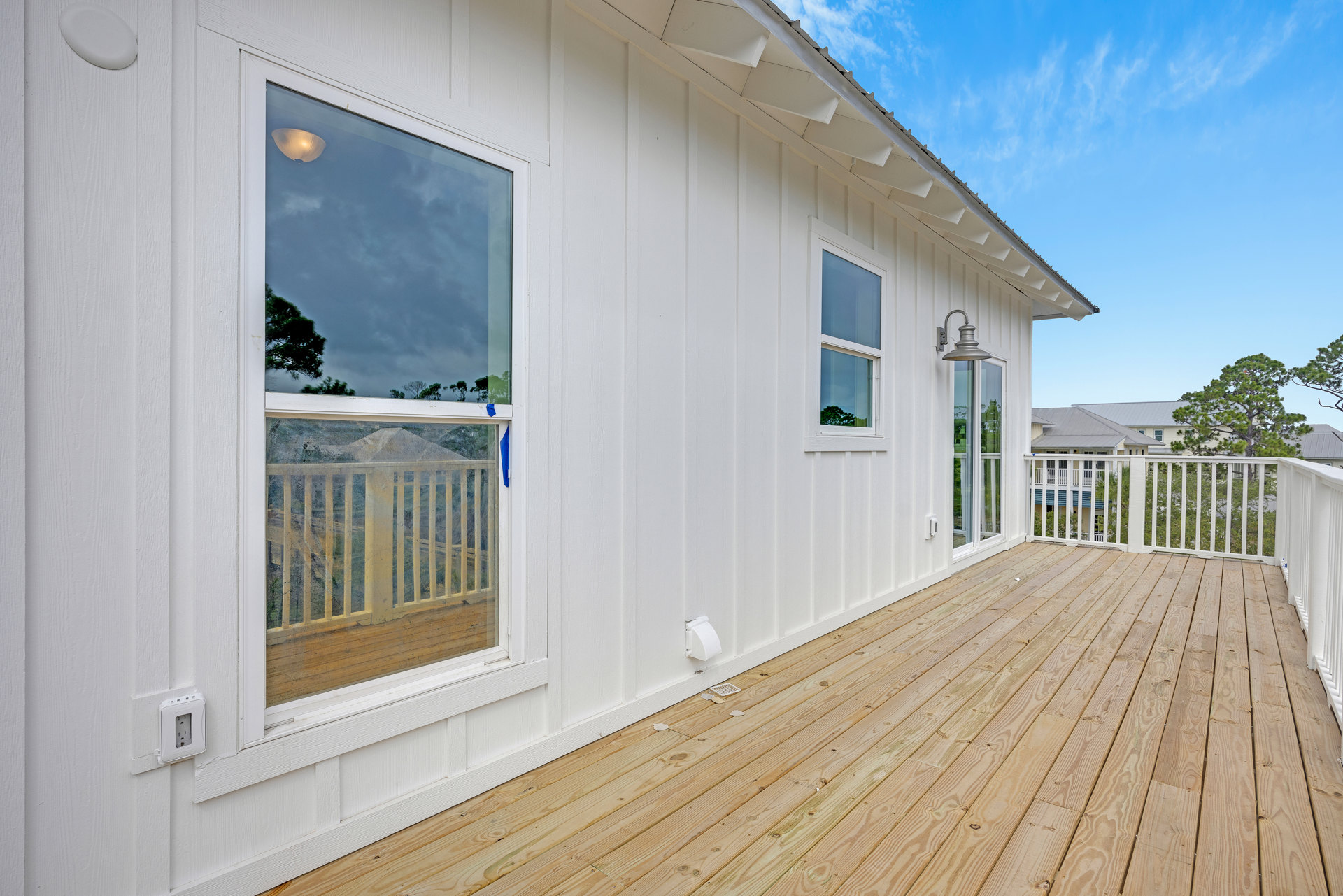 White two-story house with white siding, wooden deck, upper balcony with white railing, large windows, and outdoor light fixture.