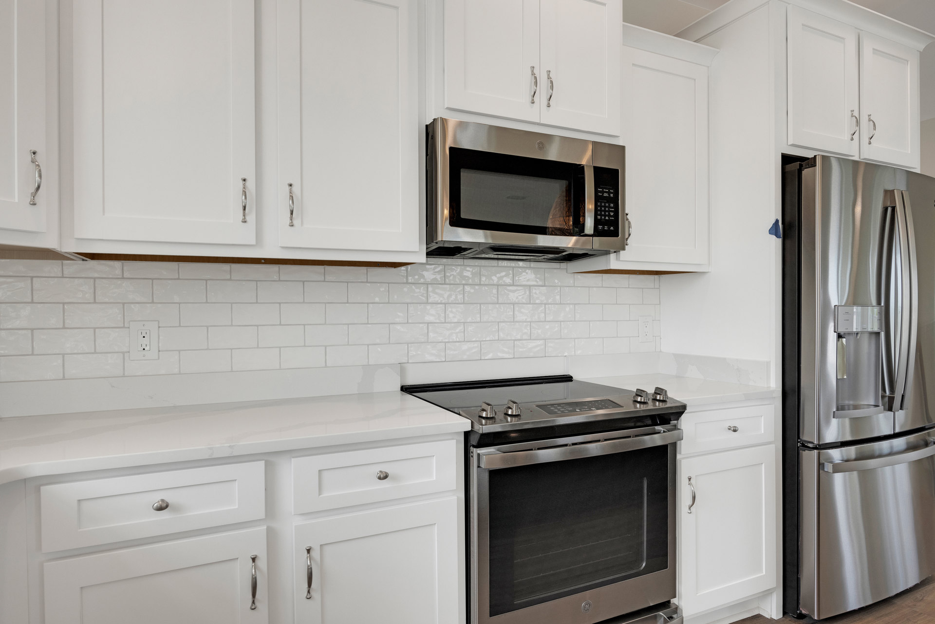 White shaker cabinets, stainless steel oven and refrigerator, built-in microwave with glass door, light stone countertops, modern kitchen appliances