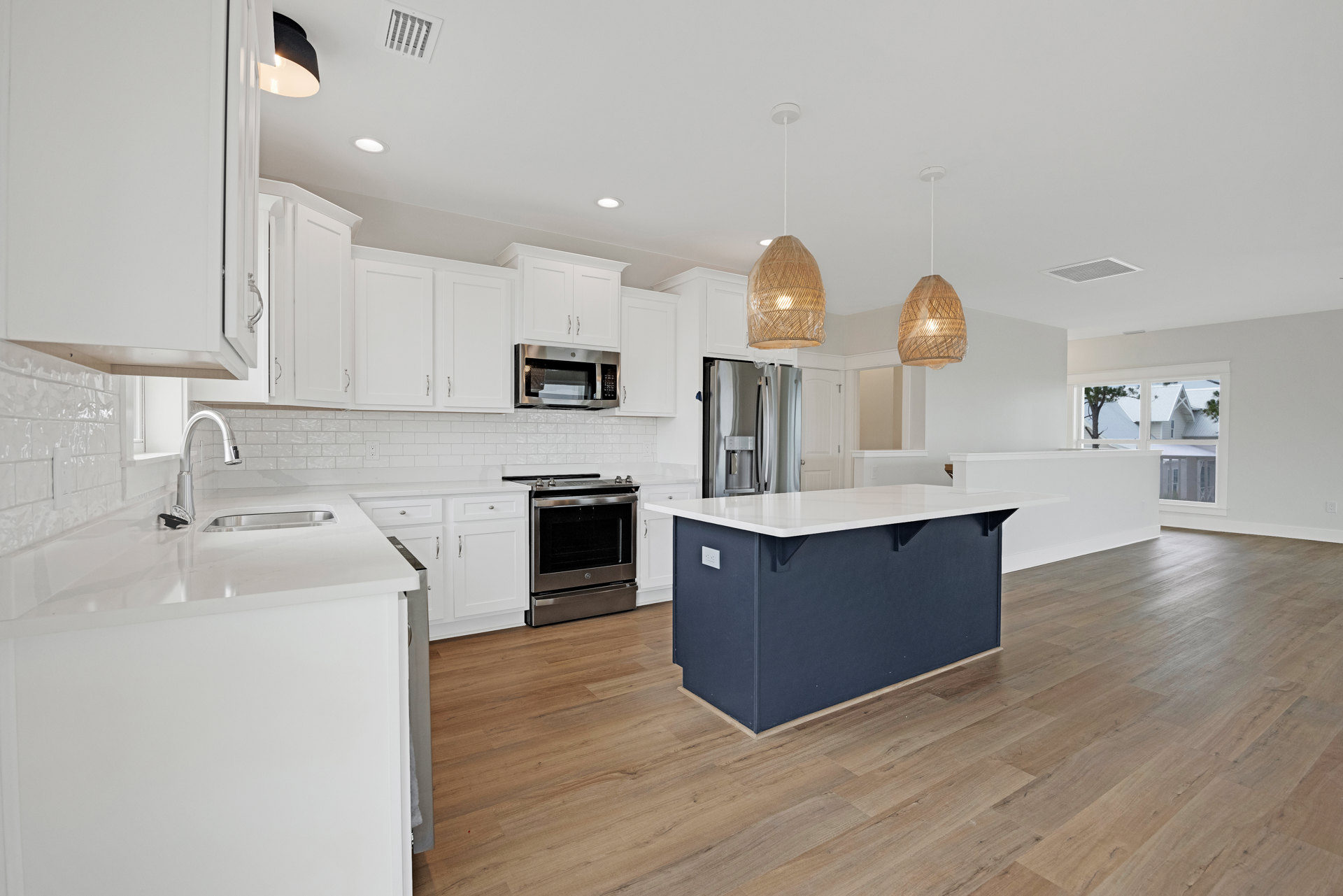 White kitchen cabinets, wood flooring, stainless steel oven with knobs, refrigerator and microwave, kitchen island with white countertop, light fixture wrapped in plastic