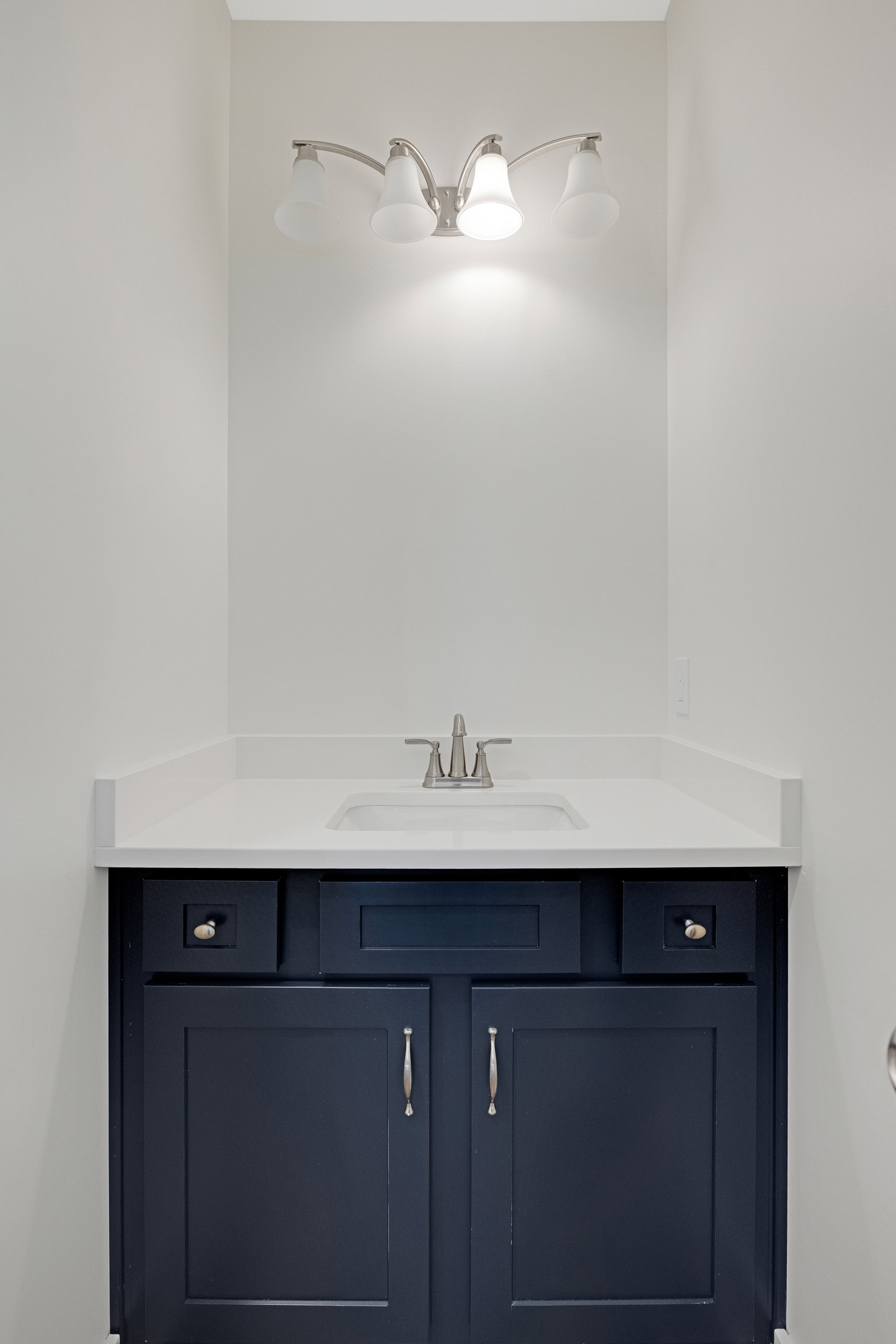 White quartz countertop with undermount sink, chrome faucet, black vanity cabinet with silver handle, and two-bulb wall sconce above.