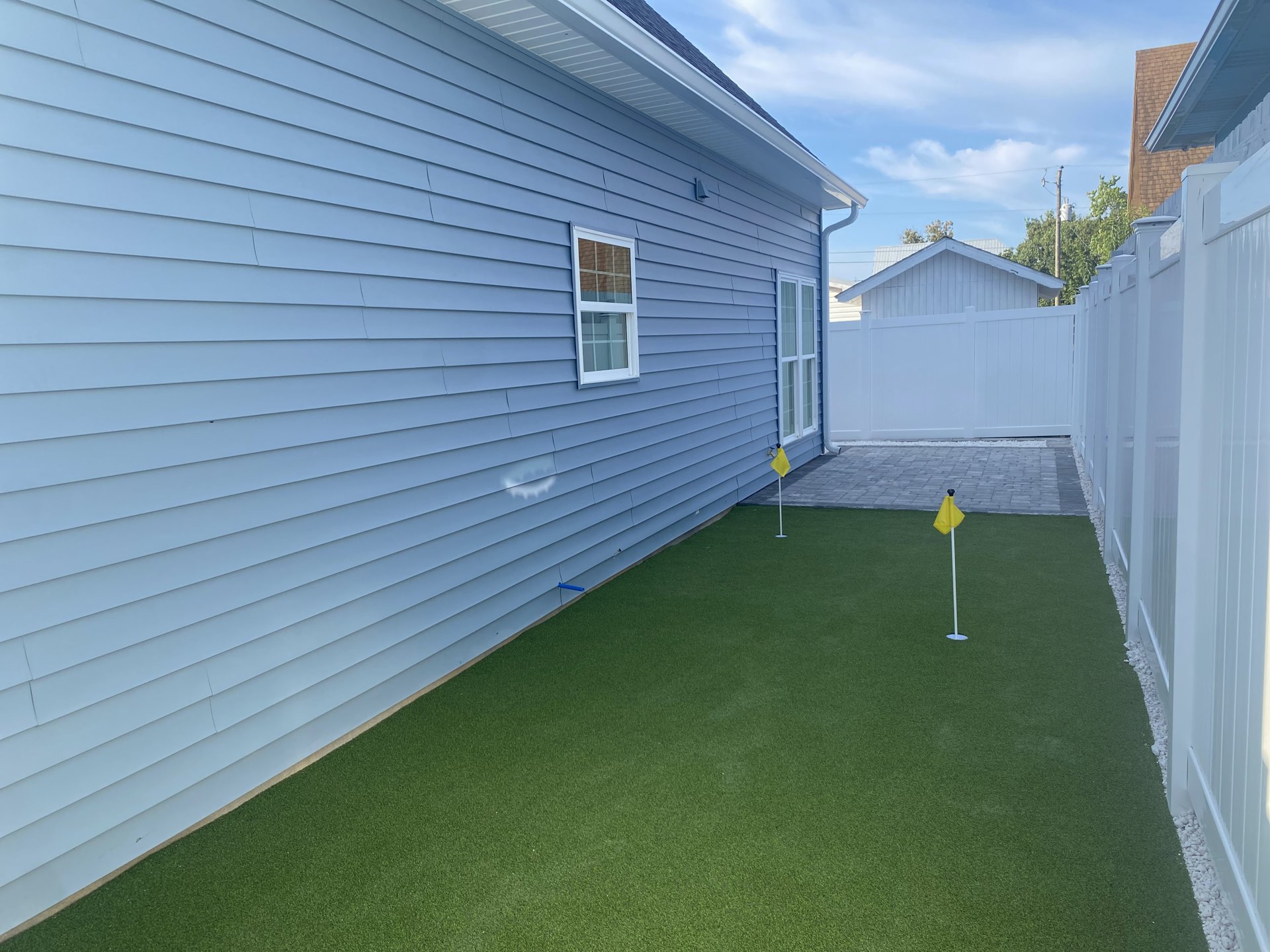 Two-story house with blue siding and brown roof, large windows, green lawn with American flag on white pole, partly cloudy sky in background
