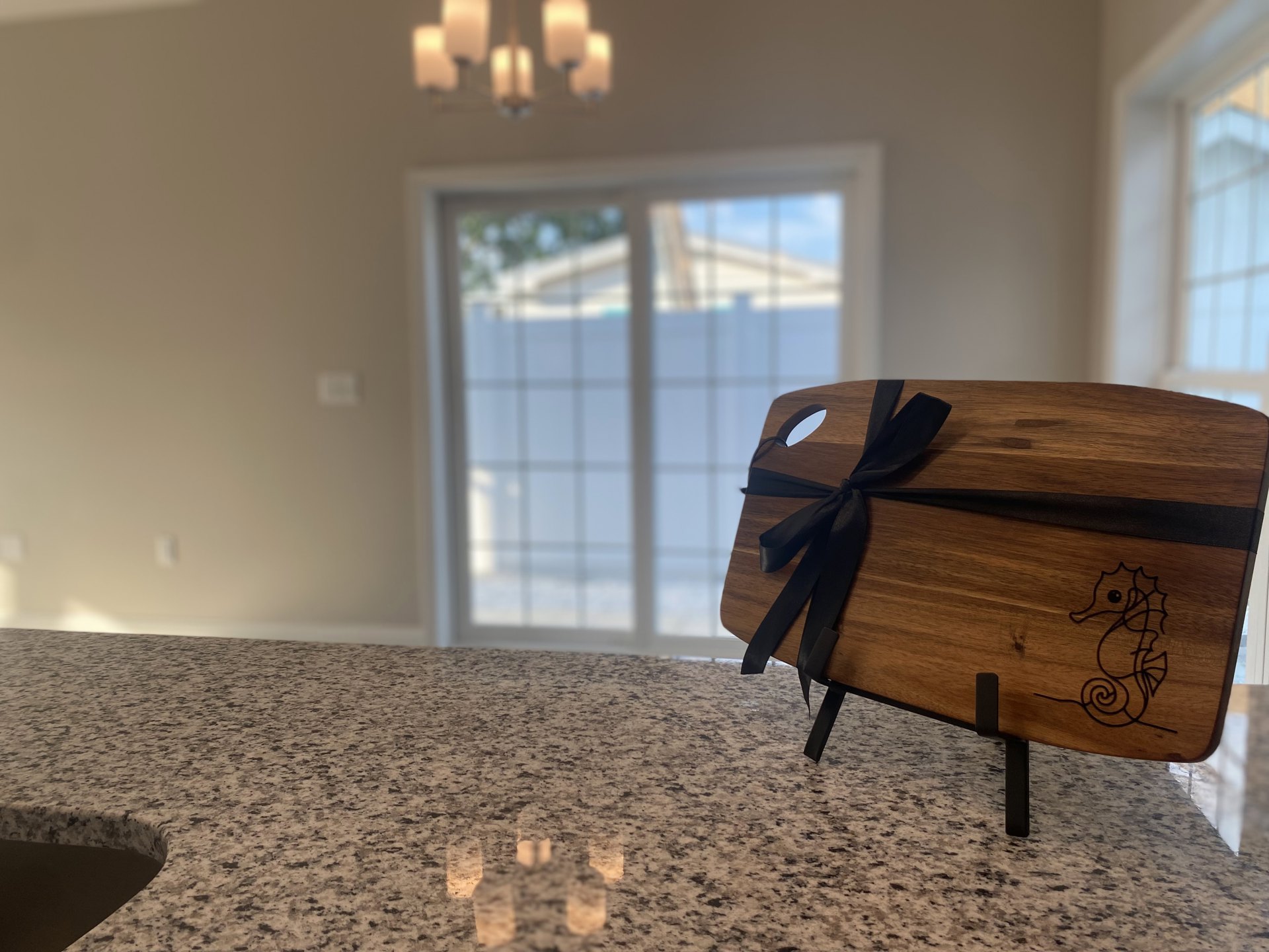 Wooden cutting board with black ribbon resting on white marble countertop, subtle reflection visible on polished surface
