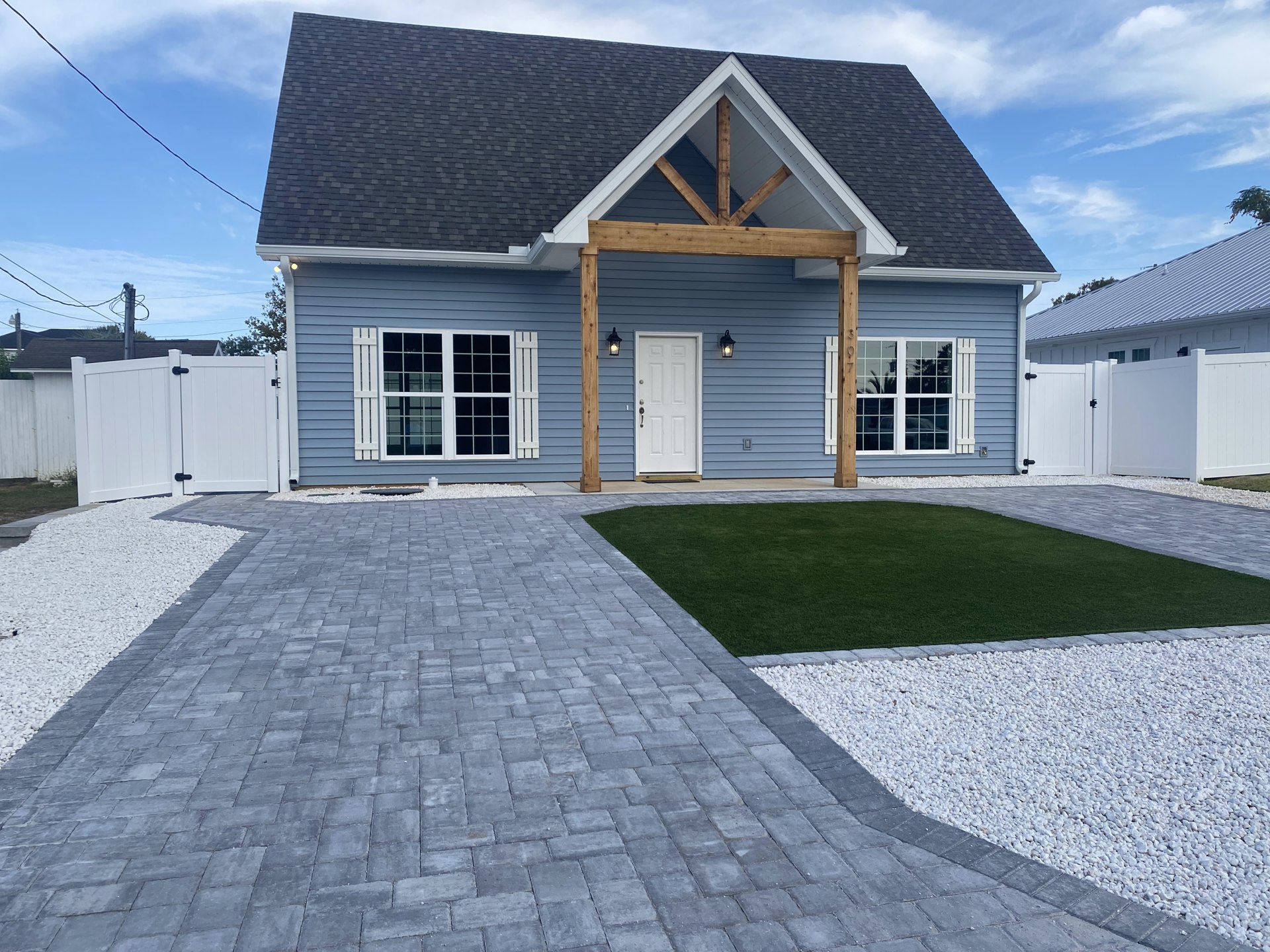 Two-story house with wooden siding, white-trimmed windows, white front door, stone walkway, green grass lawn, and paved driveway under a partly cloudy sky