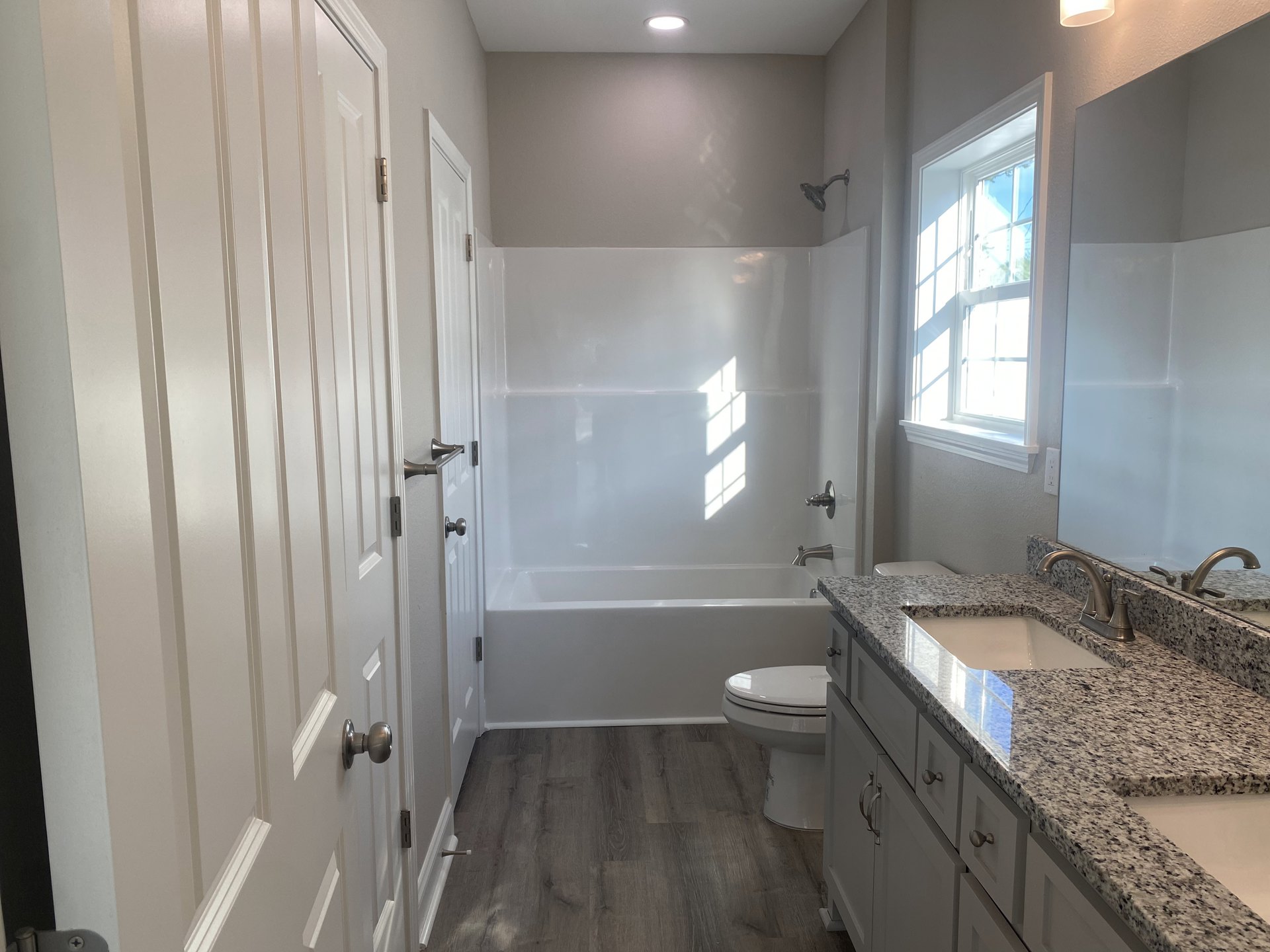 Bathroom with marble countertop and undermount sink, white bathtub, closed toilet, chrome shower head, white-framed window, light tile walls and floor.