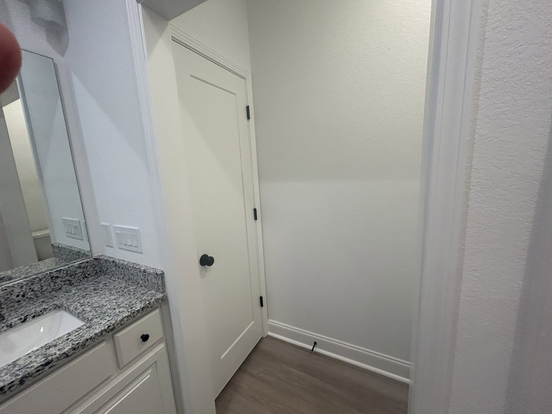 White door with black hinges set in a tiled bathroom, featuring a white sink, mirror, and light-colored cabinetry.