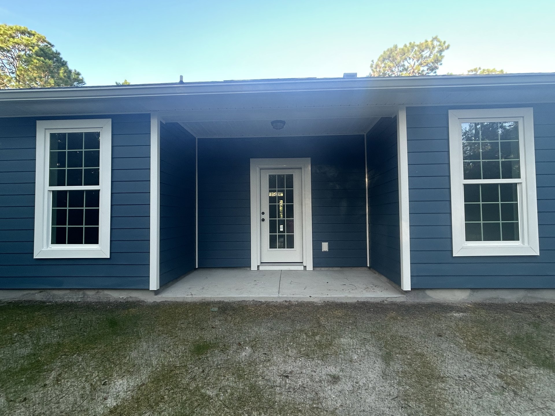 Blue siding house with white trim, white framed sash windows, white door with glass panes, front porch, green lawn, concrete sidewalk.