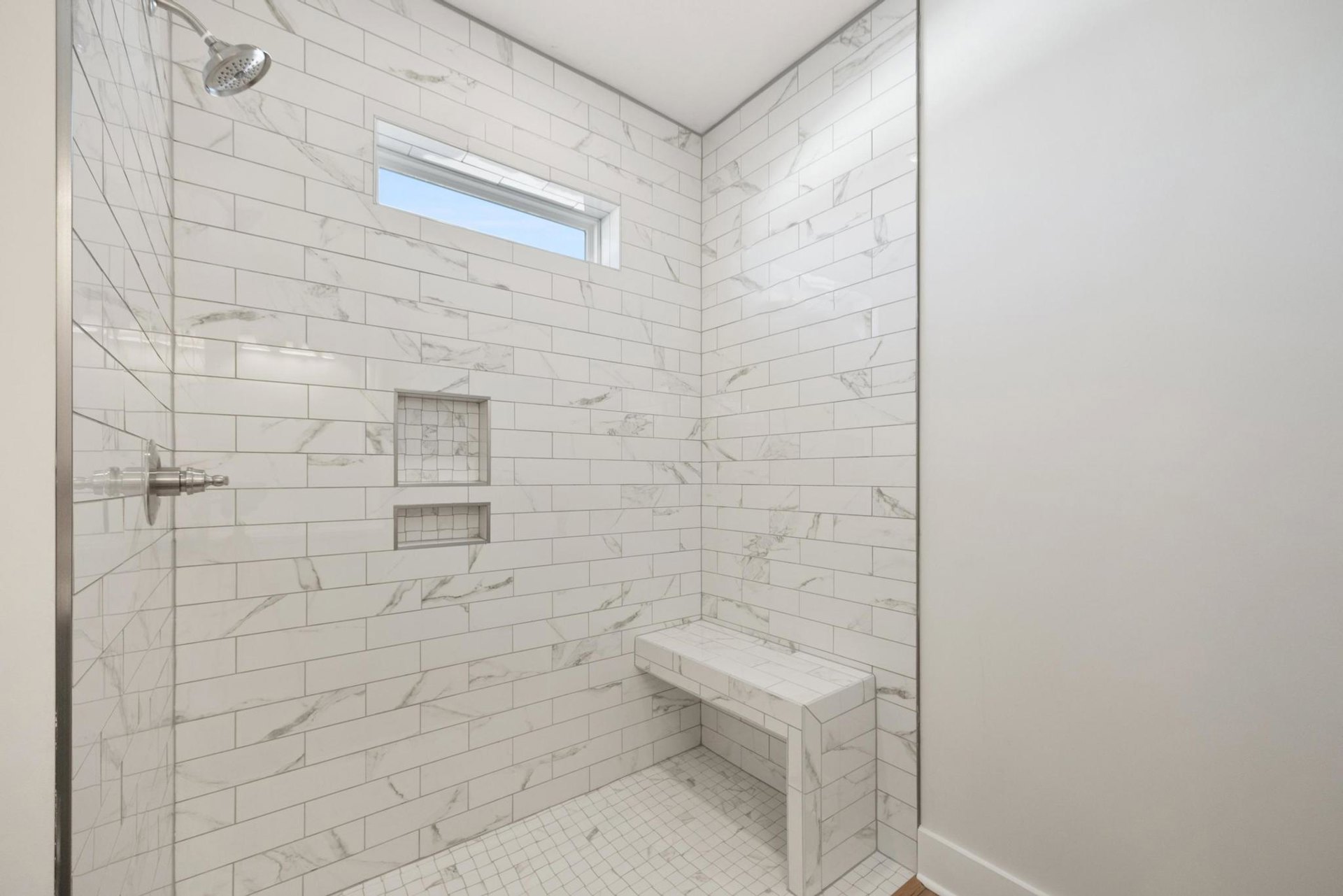 White tiled shower with built-in bench and rectangular window, marble tile walls, white border trim