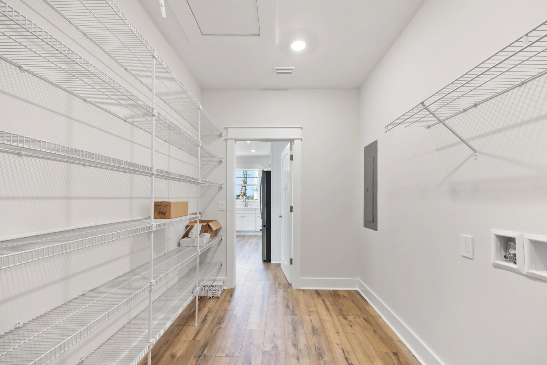 White room with built-in white wall shelves, light wood flooring, recessed ceiling light, white doors, and a brown box with black text on a shelf.