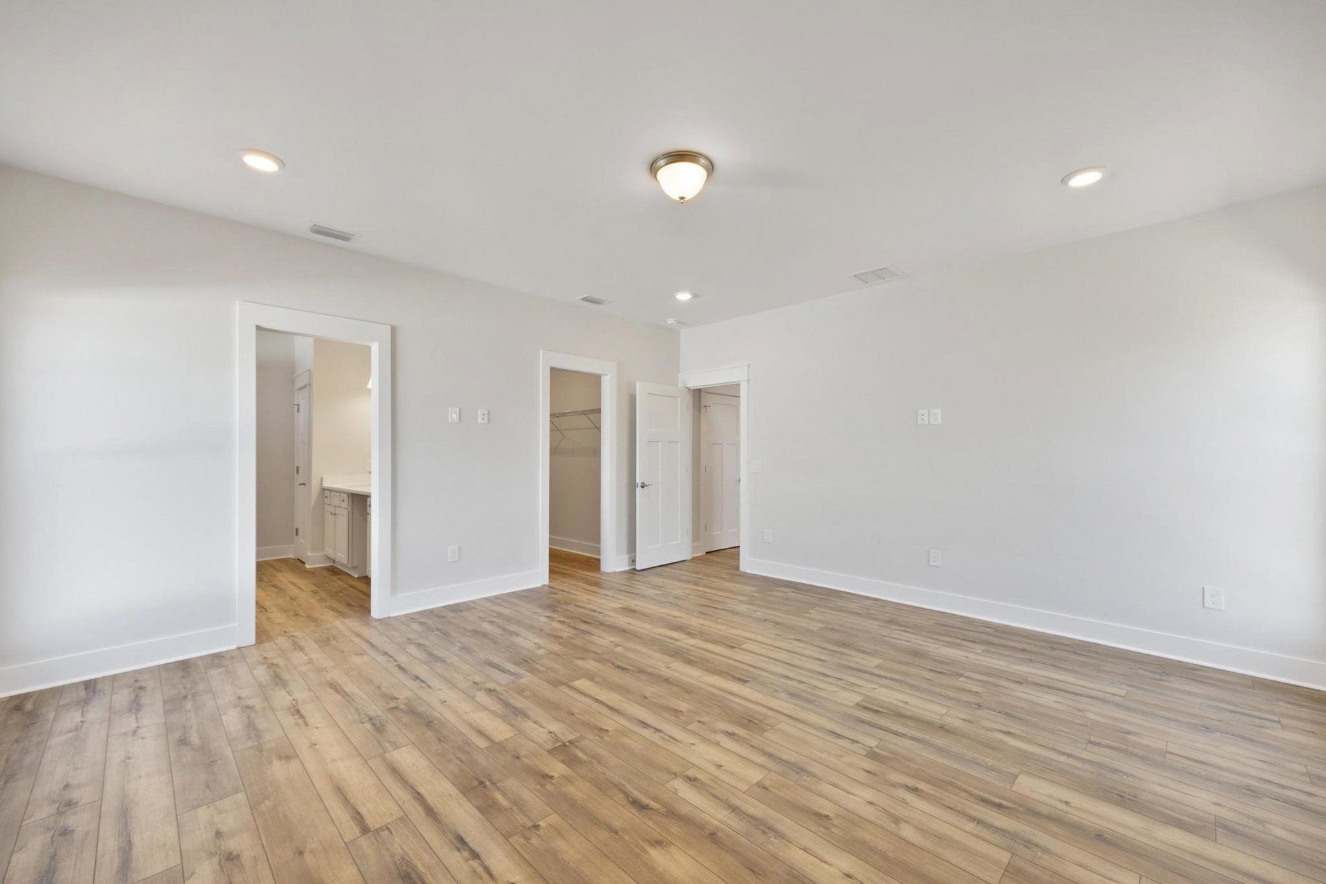 Hardwood floor with white plaster walls, white door with silver handle, ceiling light fixture