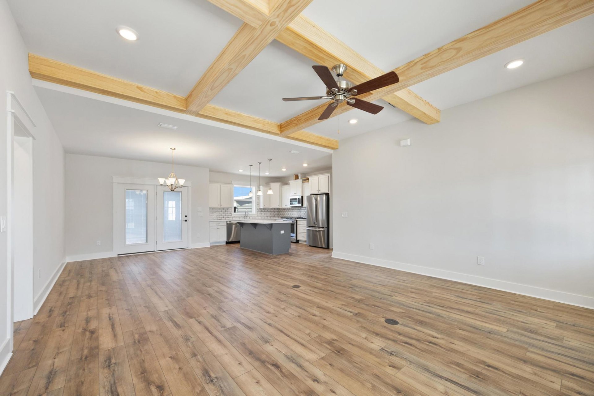 Open kitchen with wood flooring, white countertop island, stainless steel refrigerator, ceiling fan, and exposed wooden ceiling beams