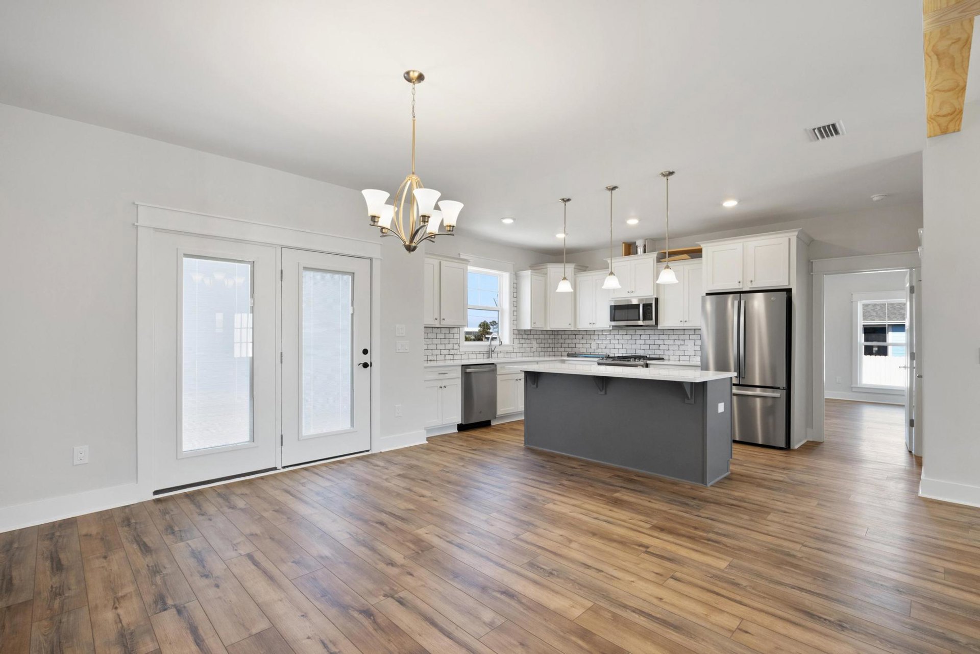 Open kitchen and dining area featuring wood flooring, stainless steel refrigerator, white countertops, grey walls, built-in microwave with black door, and large window.
