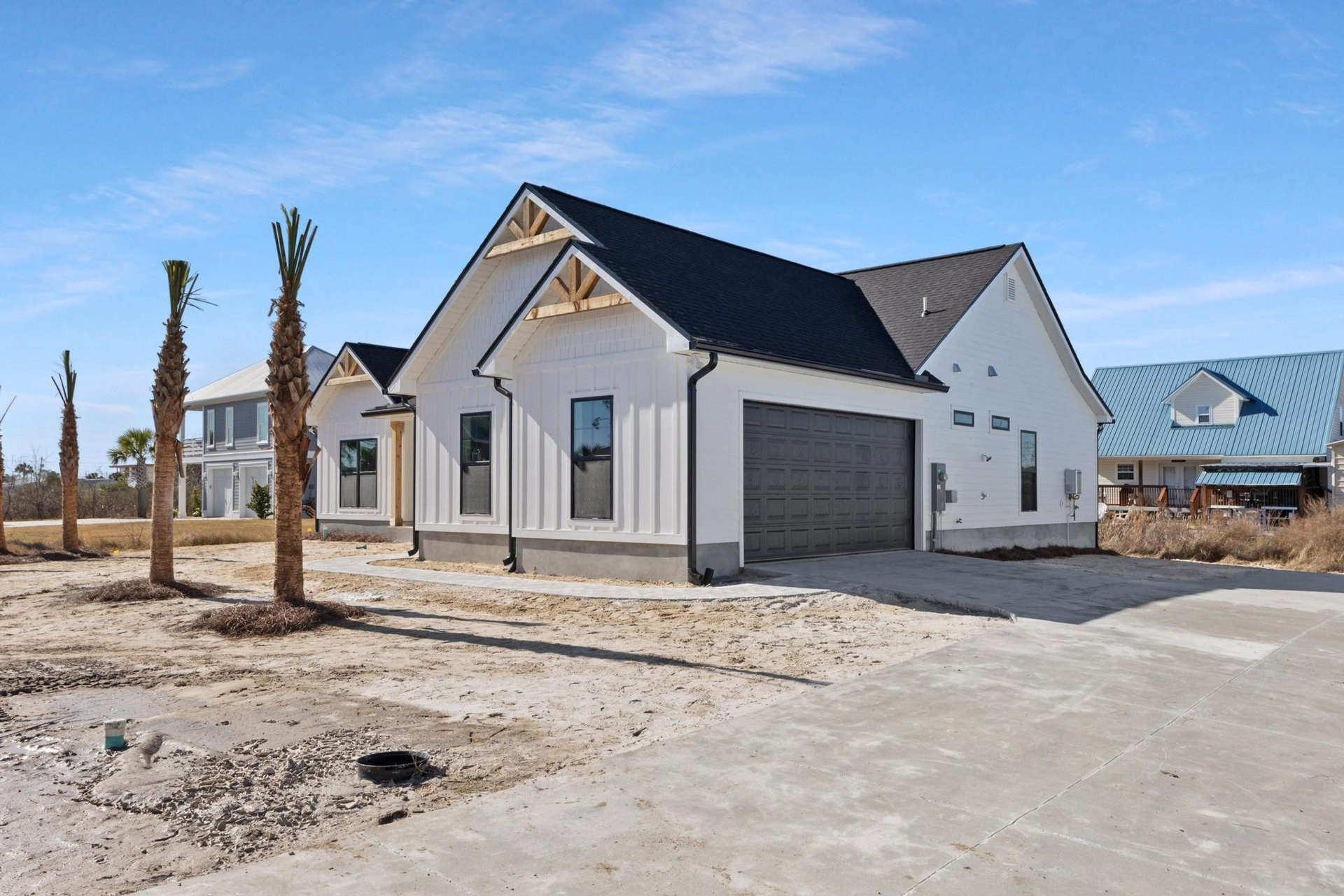 White house with black-framed windows, attached garage with paneled door, mature tree in landscaped front yard, cloudy sky overhead