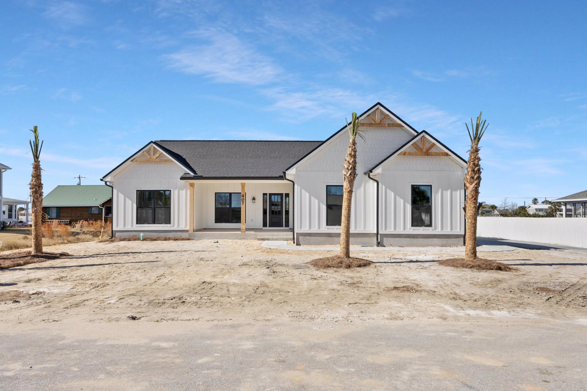 Modern home exterior with white stucco walls, black-framed windows, and a tall palm tree in the landscaped front yard