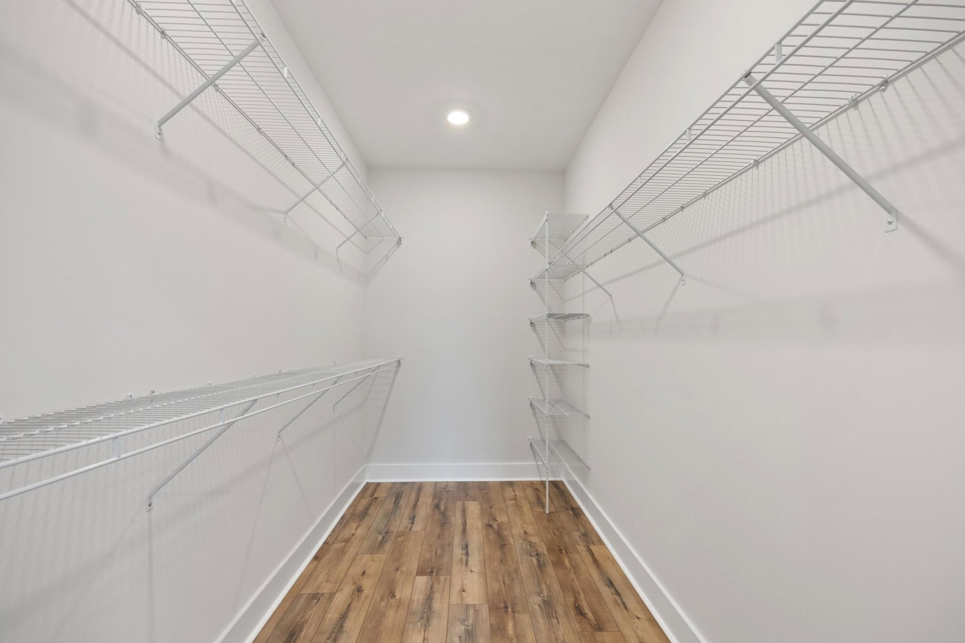 Room with white walls, wood floor, ceiling light, and built-in white shelving