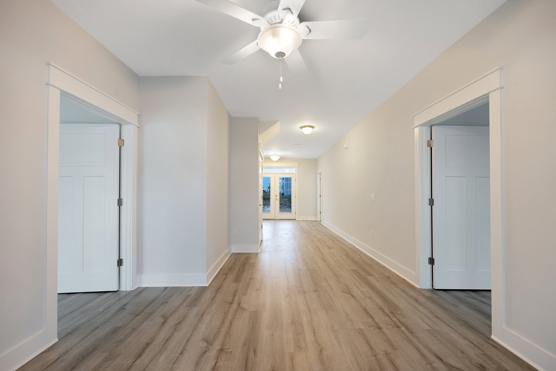White ceiling fan mounted in a hallway with wood flooring, double doors, and plaster walls