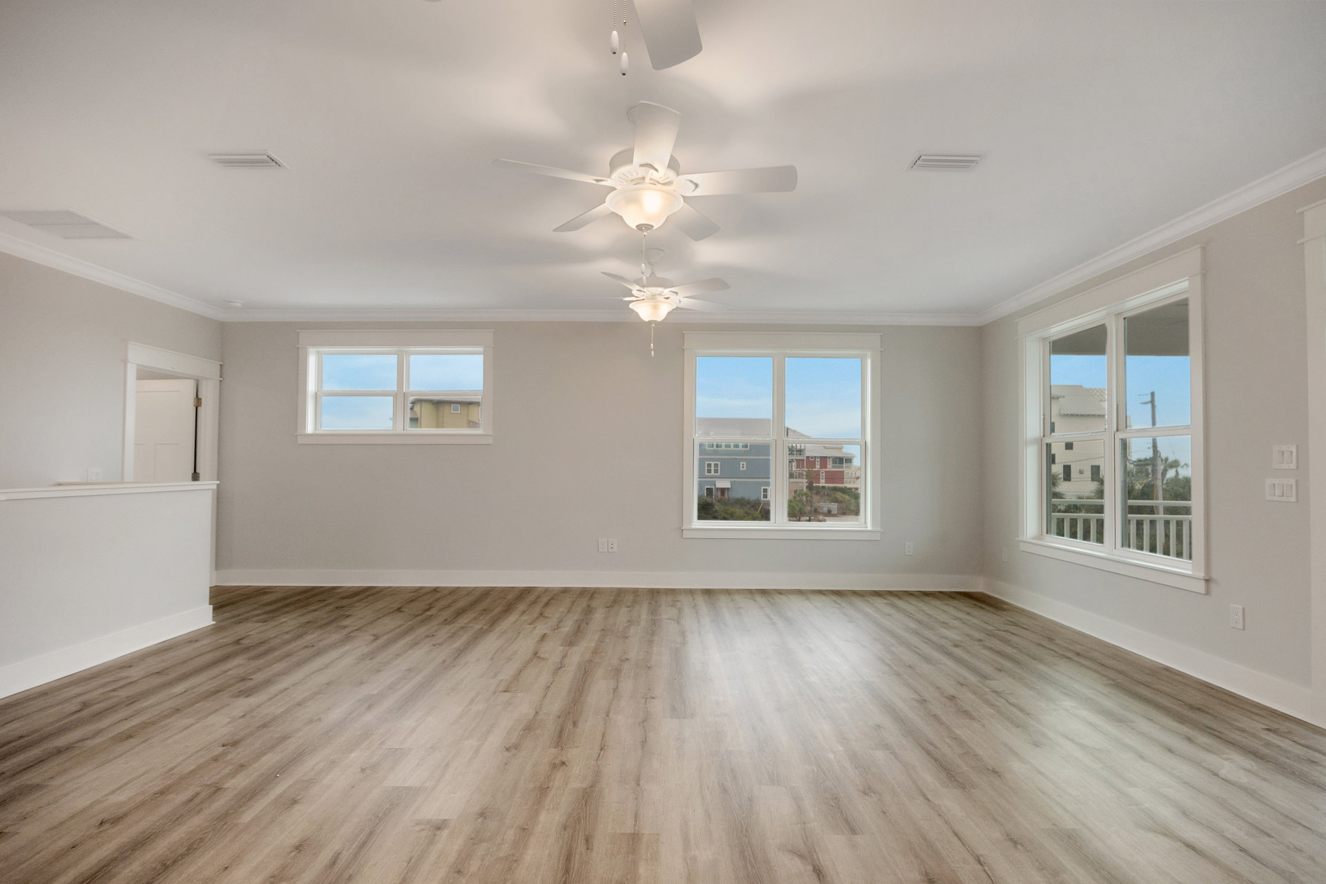 Wood flooring, white plaster walls, ceiling fan with lights, large window showing blue house and telephone pole outside