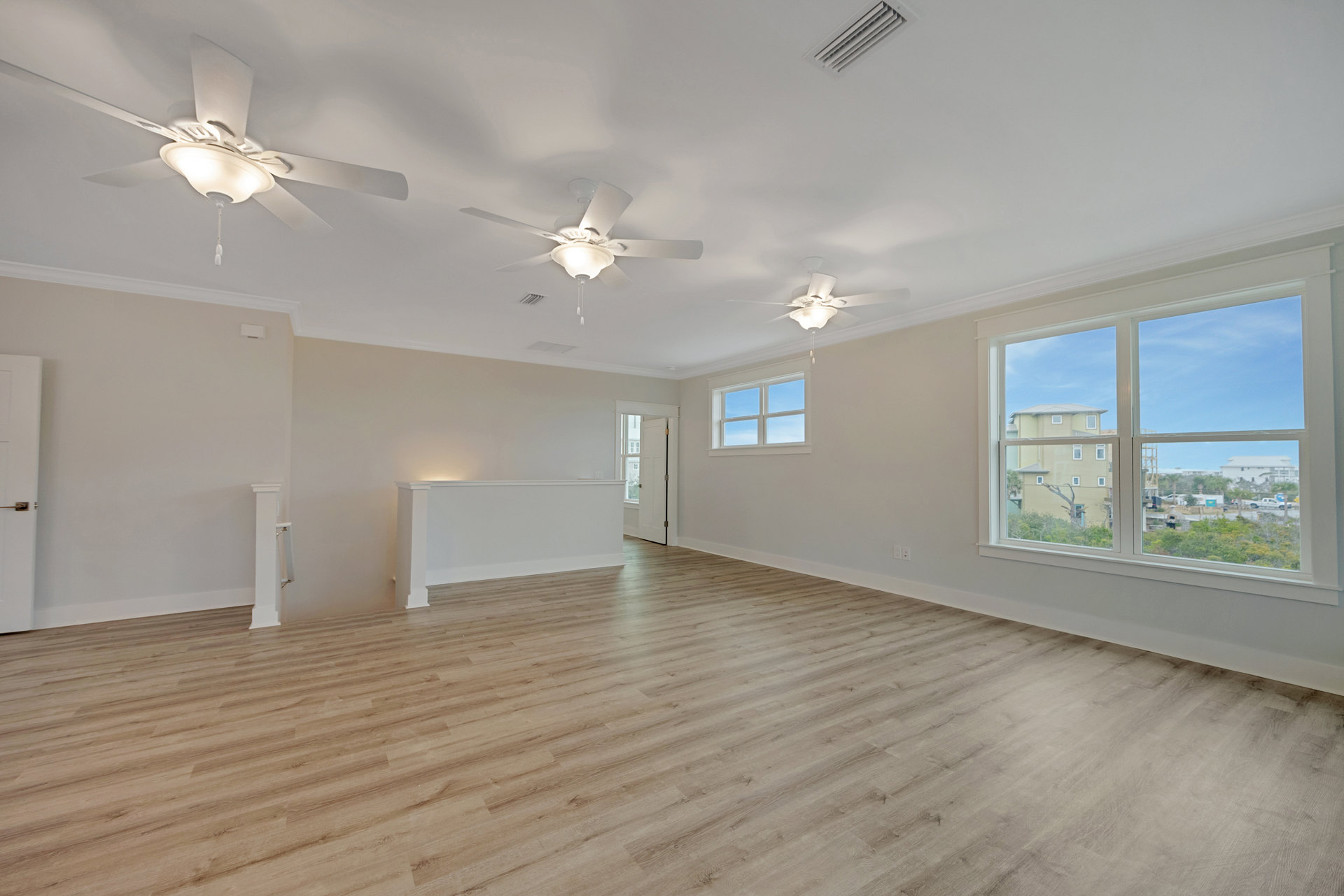 Living room with light wood flooring, white walls, ceiling fan with integrated light fixture, open doorway, and large window letting in natural light