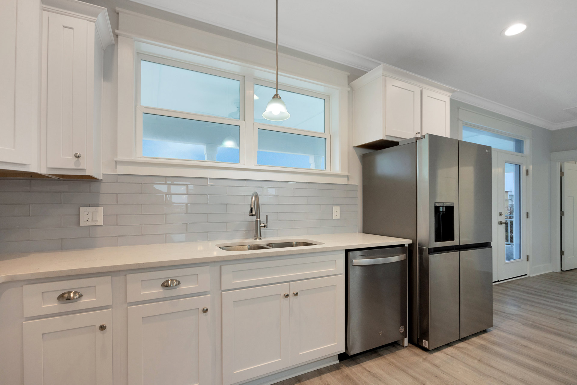 White kitchen cabinets with brushed metal handles, stainless steel refrigerator with open door, silver handle, white outlet on backsplash, square-framed cabinet doors, light stone