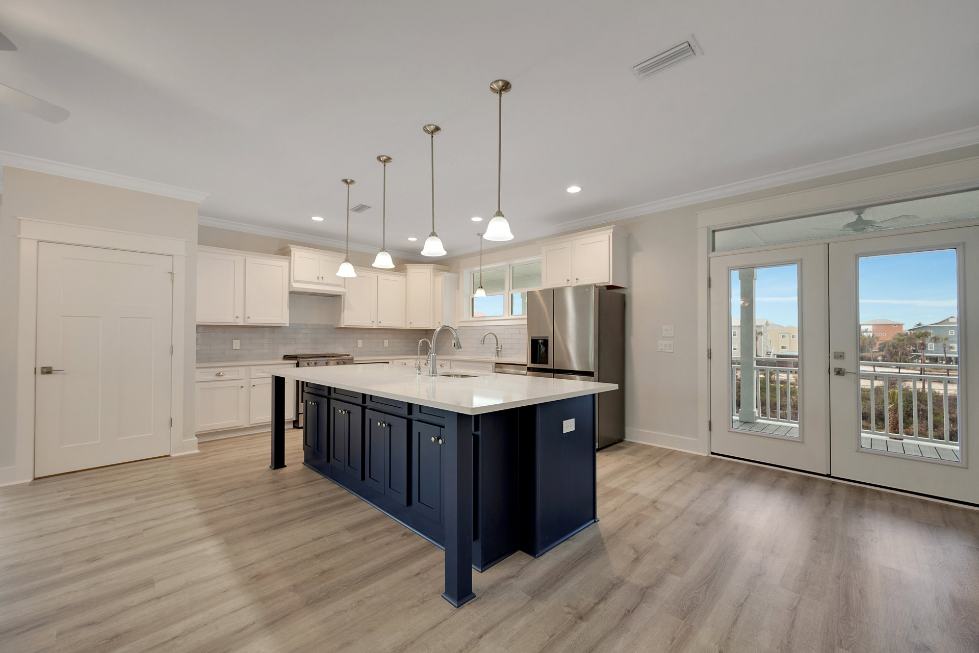 Open kitchen with white cabinetry, central island featuring a sink, stainless steel stove and appliances, glass double doors, light fixture with white shade, and wood flooring.