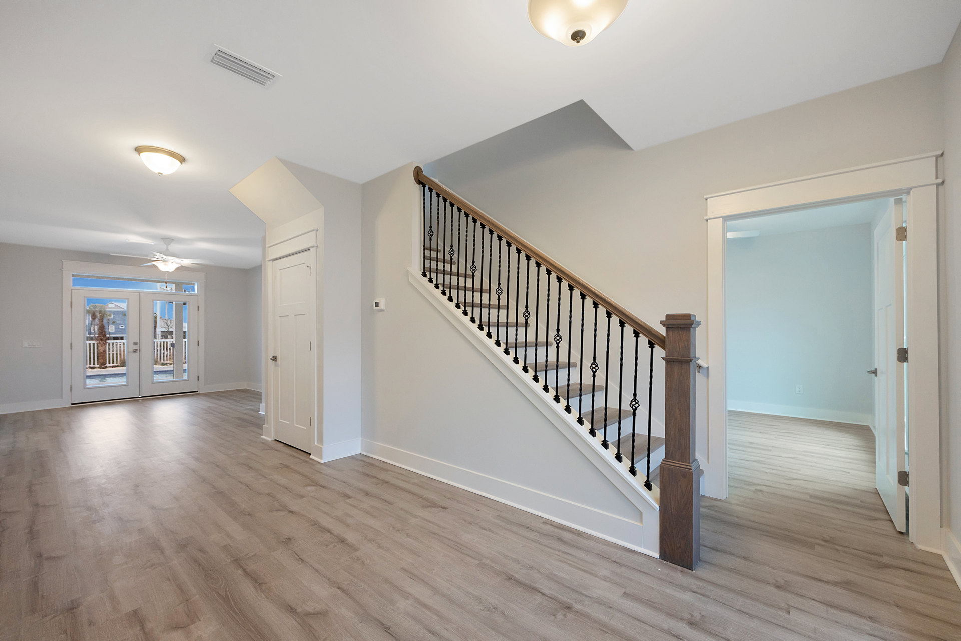 Wood staircase with black metal railings, glass-paneled double doors, white walls, wood flooring, and a close-up of a modern light fixture
