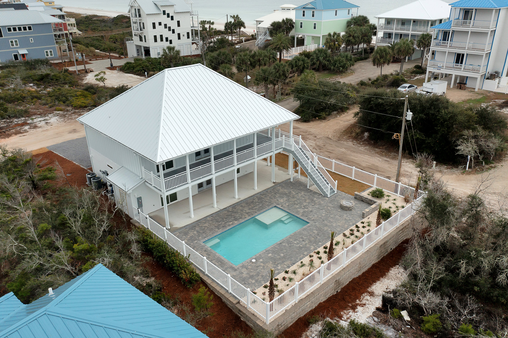 White house with a white roof, surrounded by trees, featuring a central swimming pool with a built-in slide and steps, bordered by a white fence.