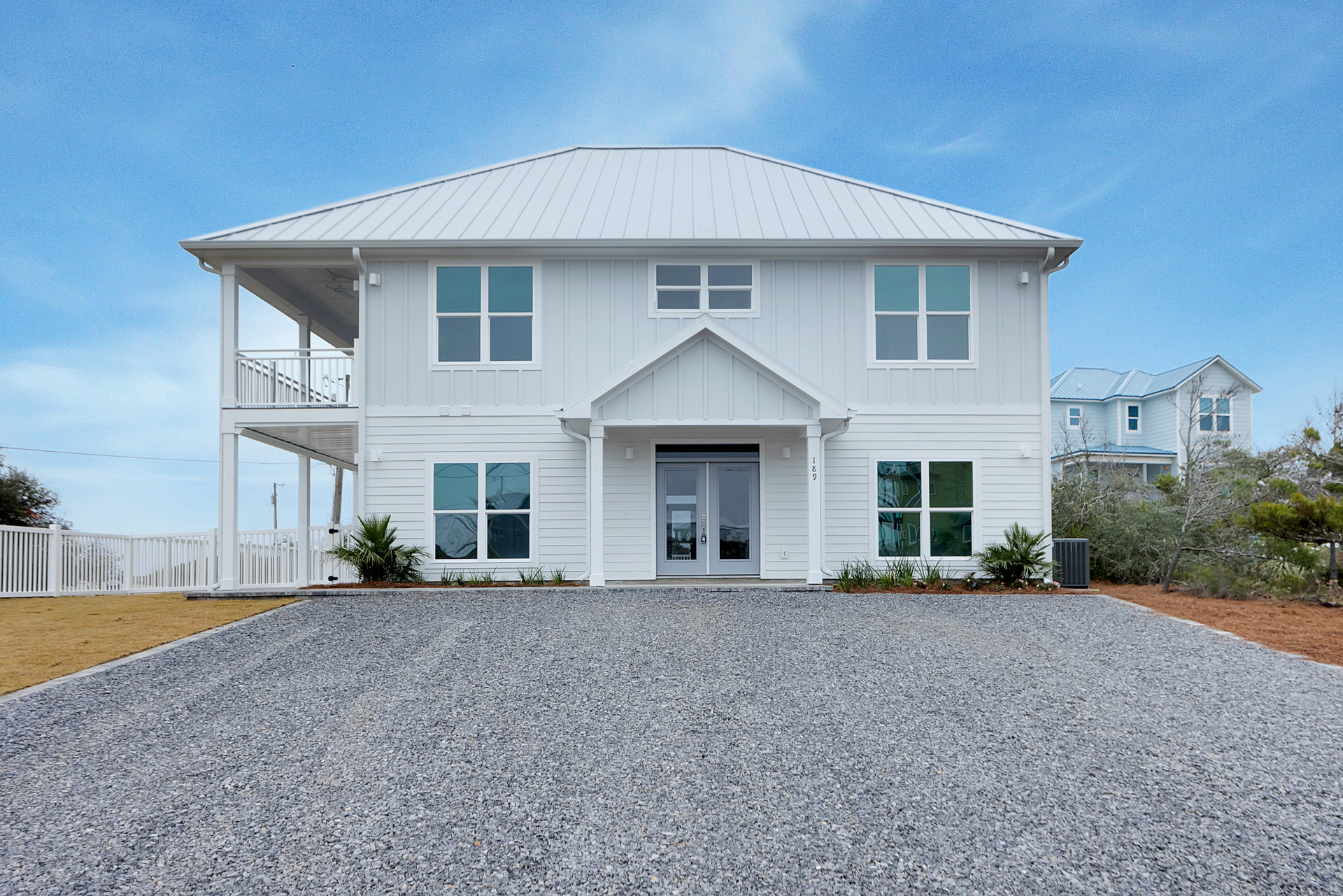 White exterior home with gravel driveway, grey double front doors with glass panels, large windows, and blue sky above