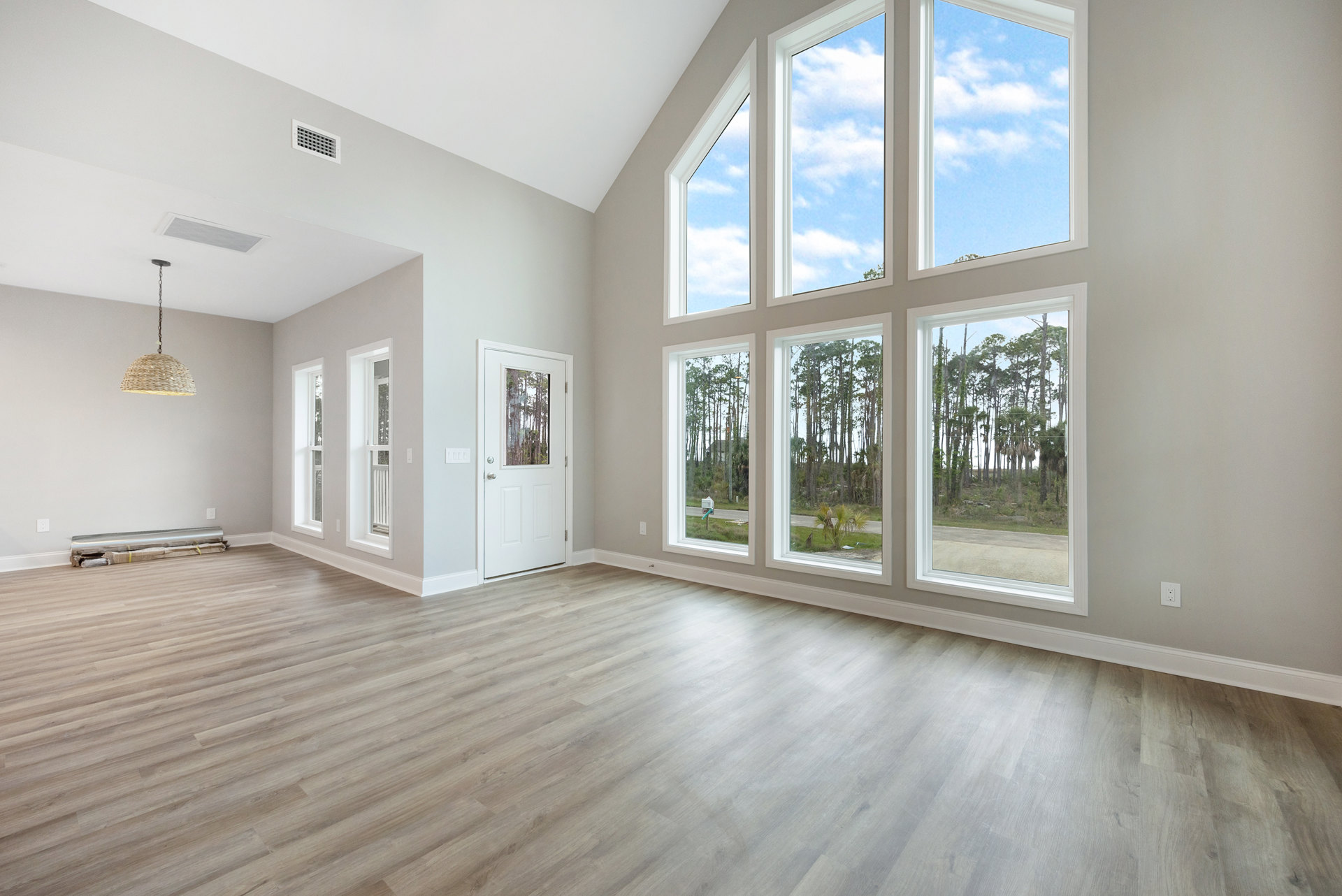Spacious room featuring large windows, hardwood flooring, white walls, and a white door with glass panel