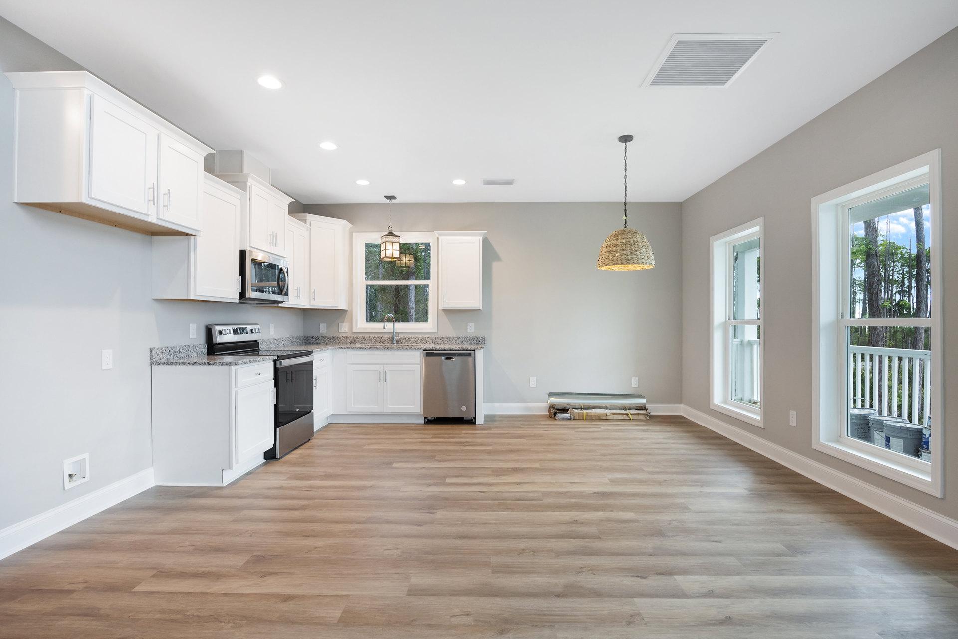White kitchen cabinets, stainless steel appliances, wood plank flooring, quartz countertops, recessed ceiling vent, and modern light fixture.