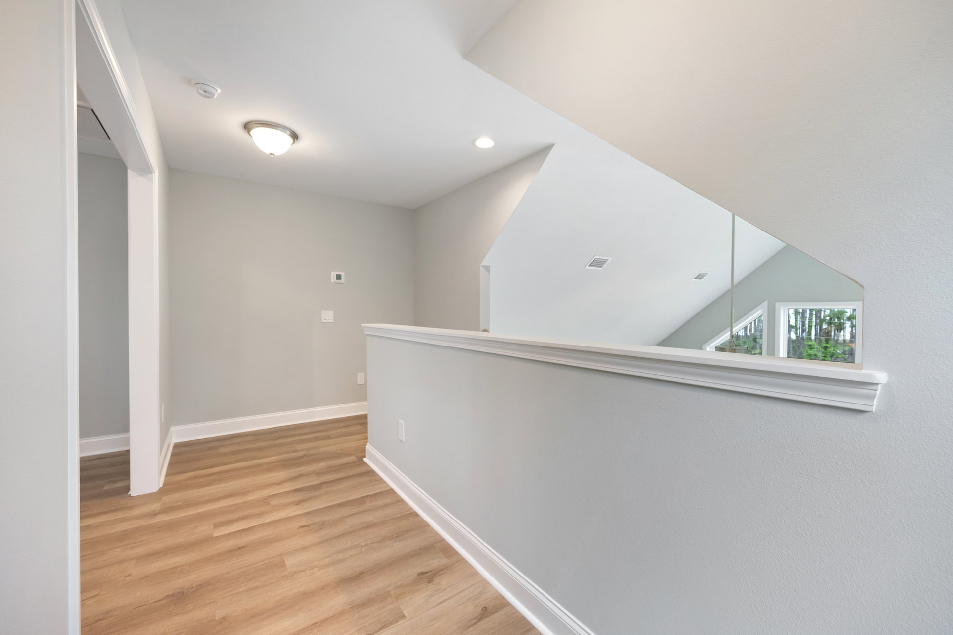 Hallway with warm wood flooring, white plaster walls, modern light fixture, ceiling vent, and window overlooking trees