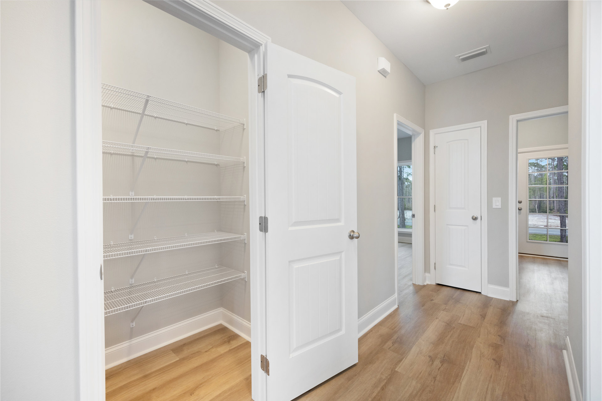 Open white door with silver handle and glass panes leading to a room with built-in white shelving, laminate flooring, and plaster walls