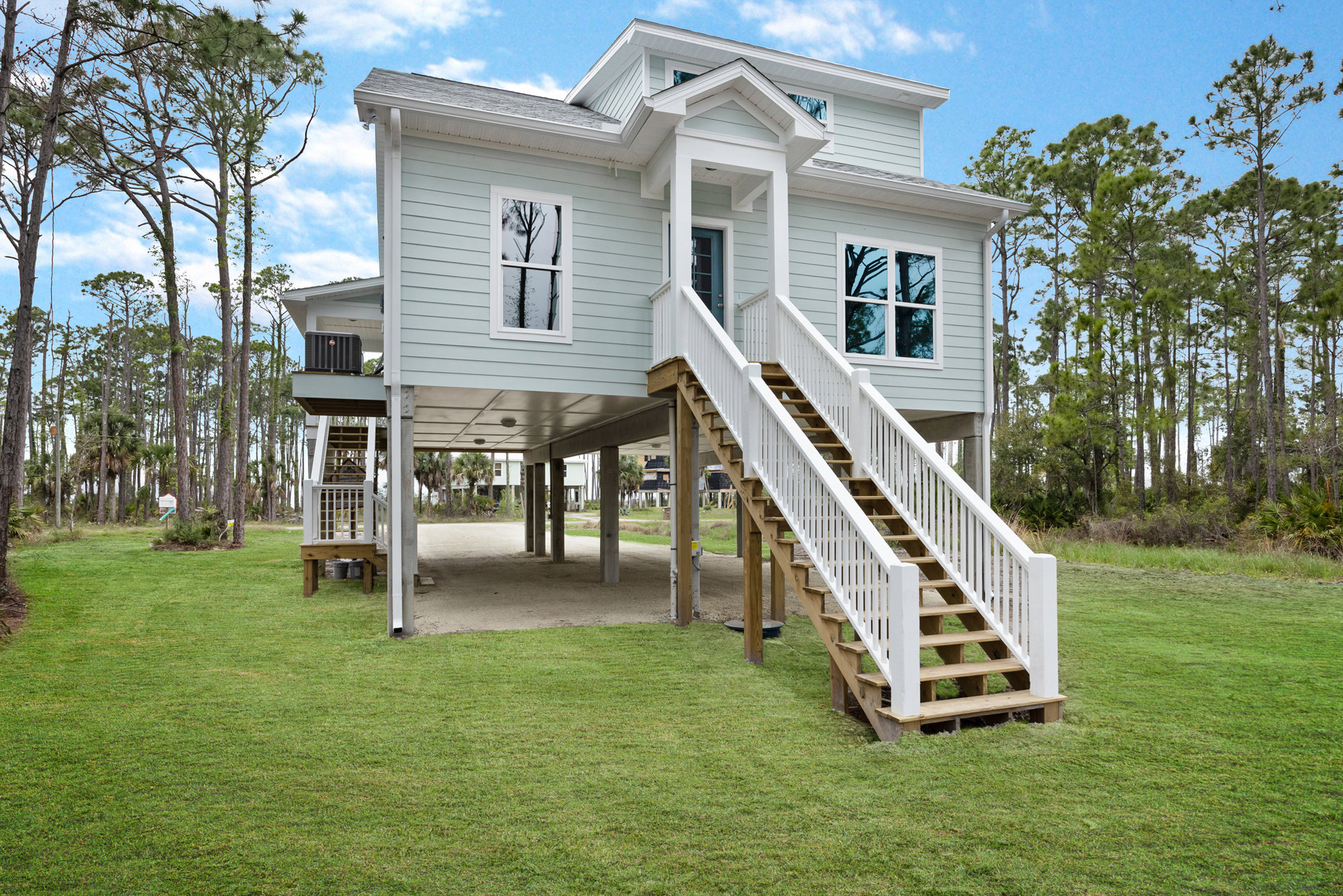 Two-story house with white siding, covered front porch, wooden stairs, large windows reflecting nearby trees, manicured lawn, and outdoor air conditioning unit.