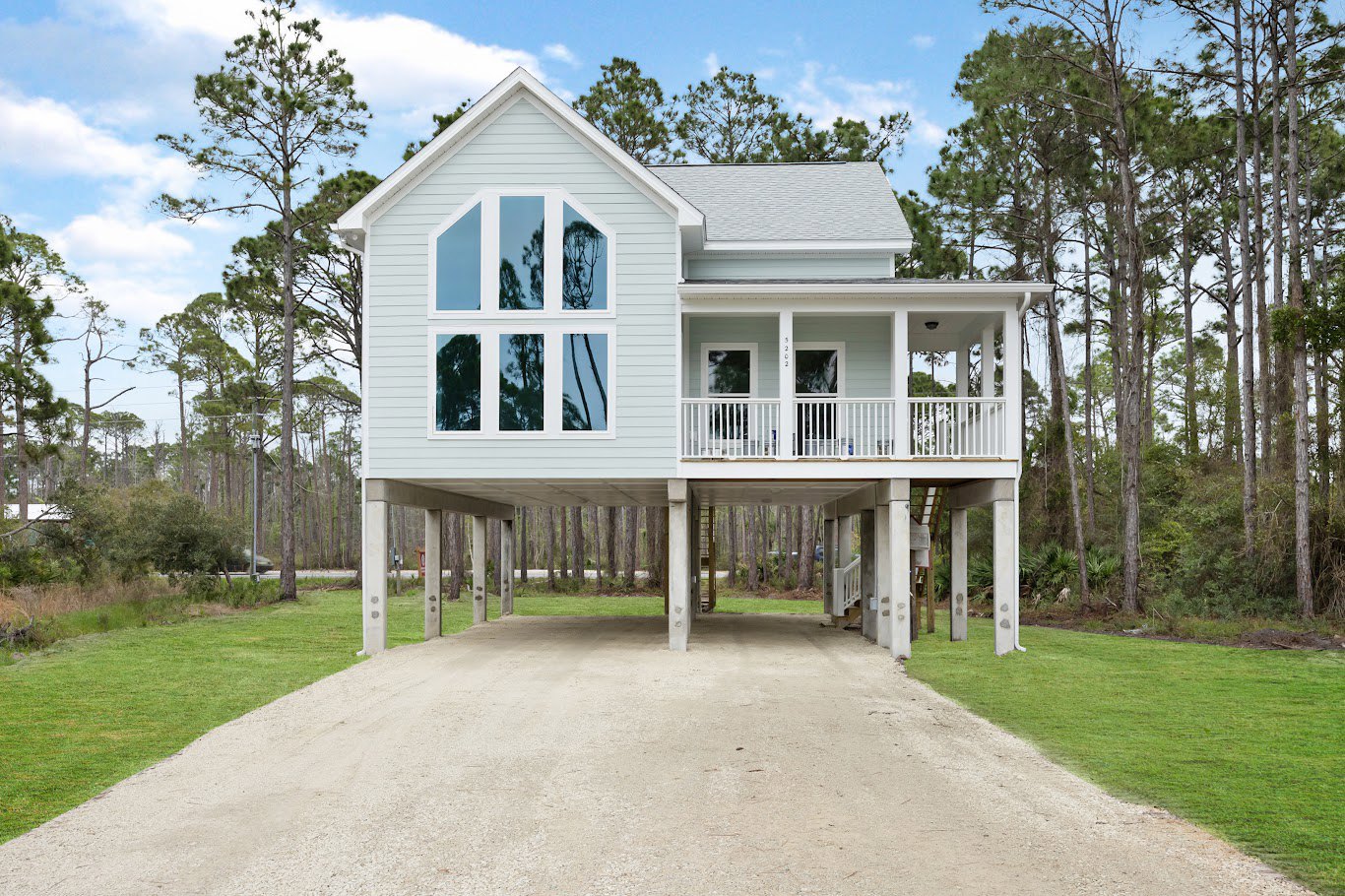 Two-story house with white-framed windows, covered front porch, concrete driveway, manicured lawn, and mature trees in the background