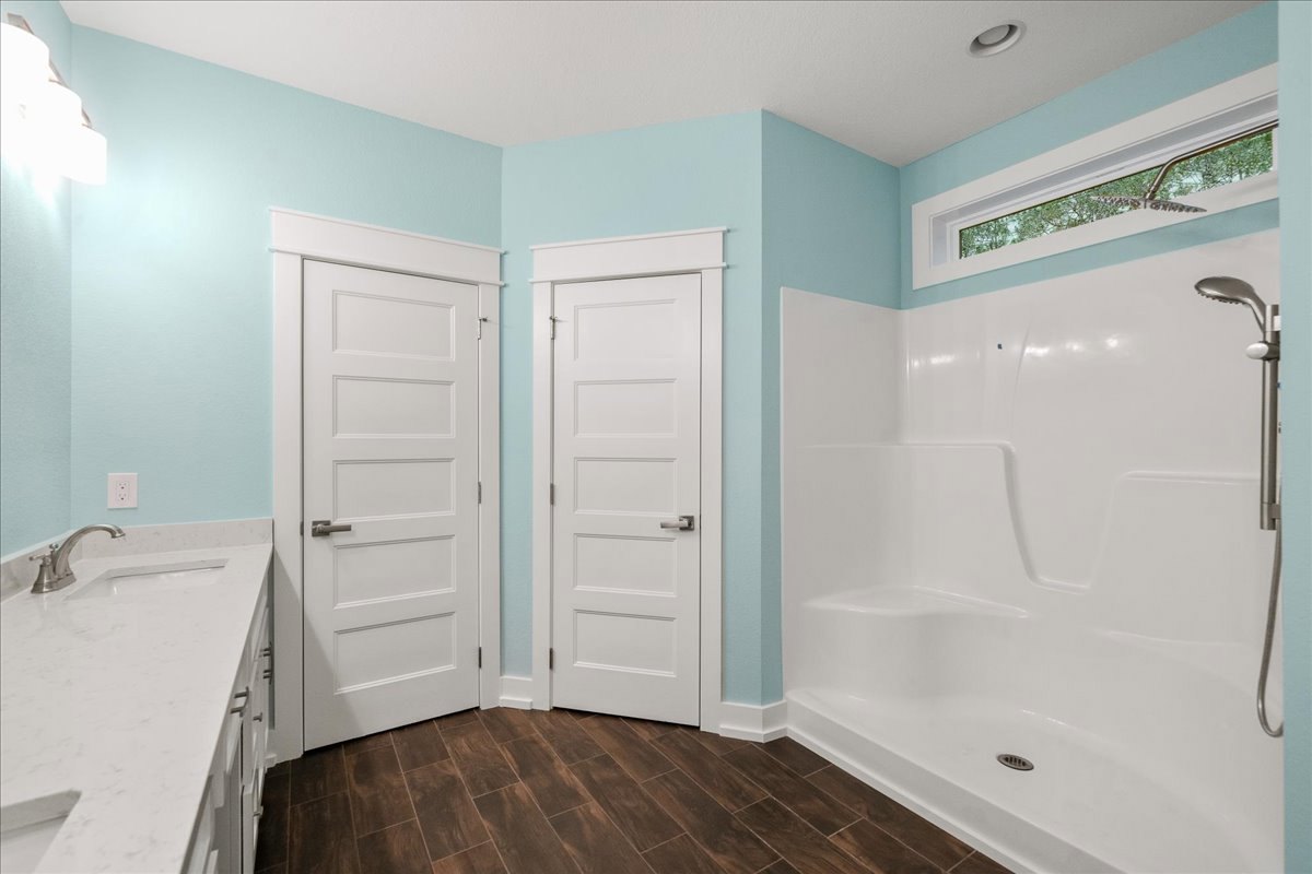White bathroom with paneled door and silver handle, glass-enclosed shower, white countertop with silver faucet, light tile flooring, and neutral wall finishes.