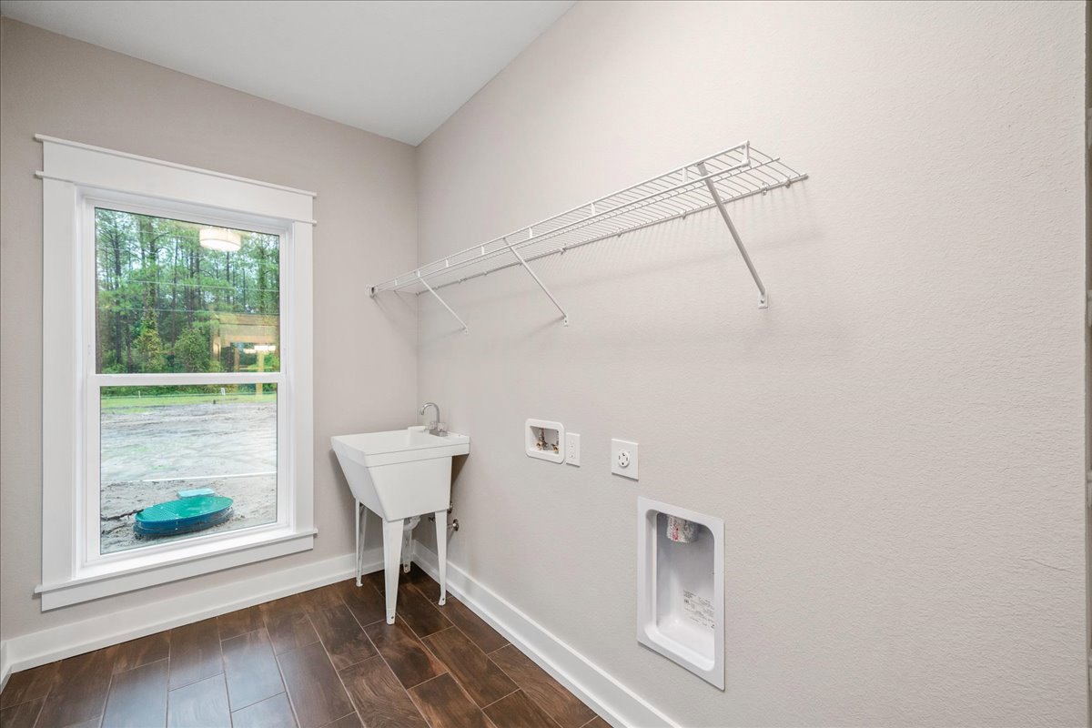 Laundry room with white sink in corner, window with white frame and green table, white shelf mounted on wall, white container with red label on countertop, light tile flooring