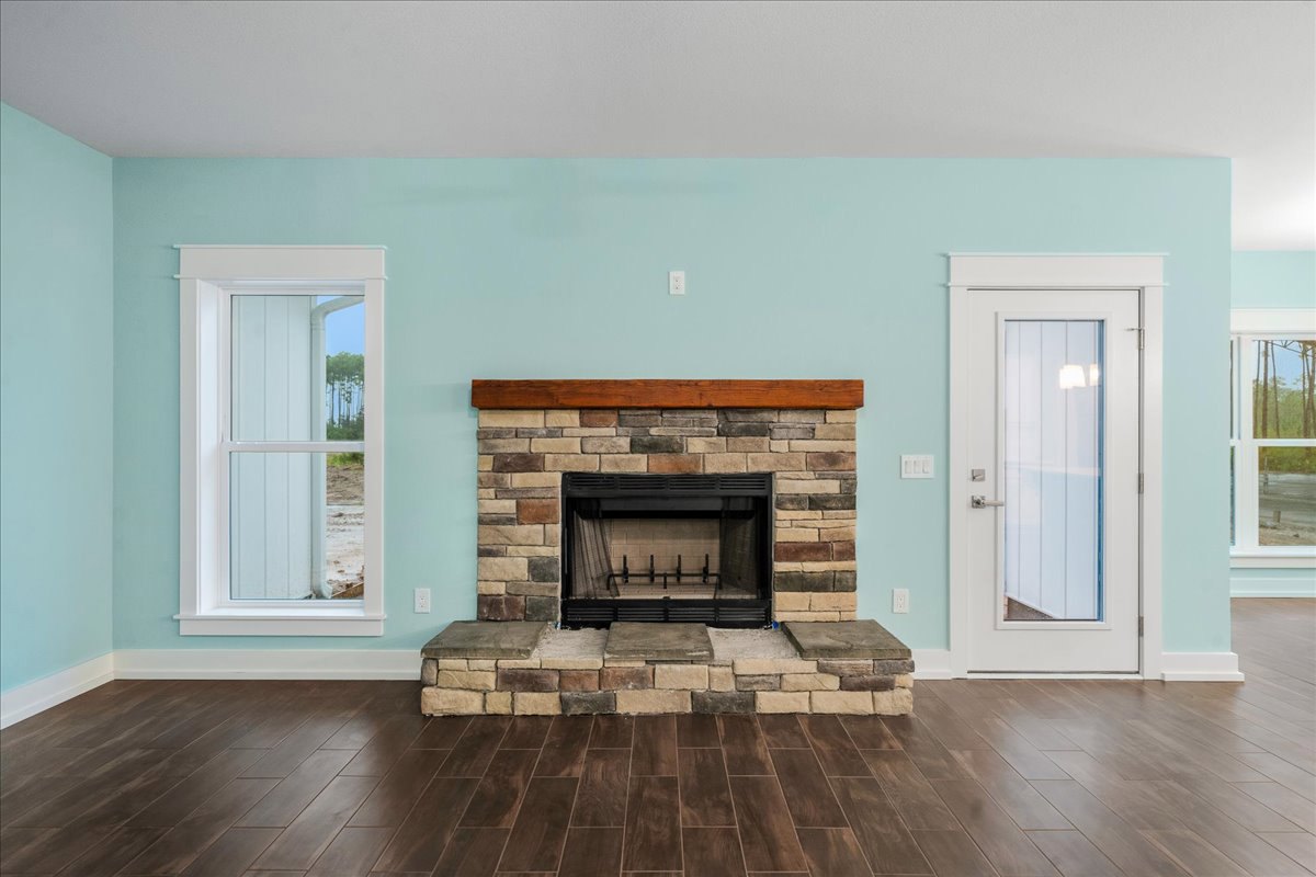 Black-framed fireplace set in a brick wall, white-framed window and glass-paneled white door, stone wall with square top, wood laminate flooring