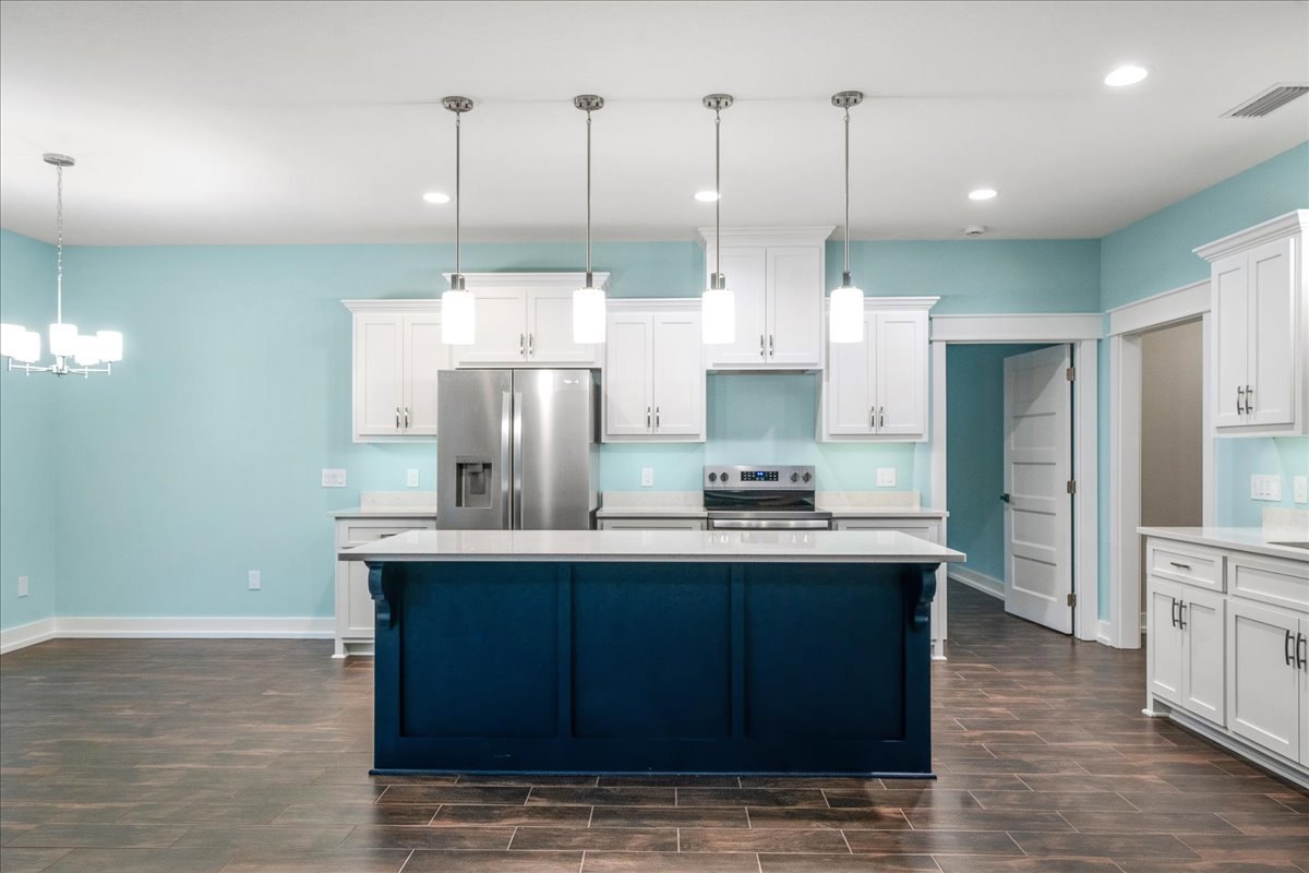 Blue and white kitchen island with marble countertop, stainless steel refrigerator, white cabinetry, tile backsplash, wood flooring, and a white door with black handle